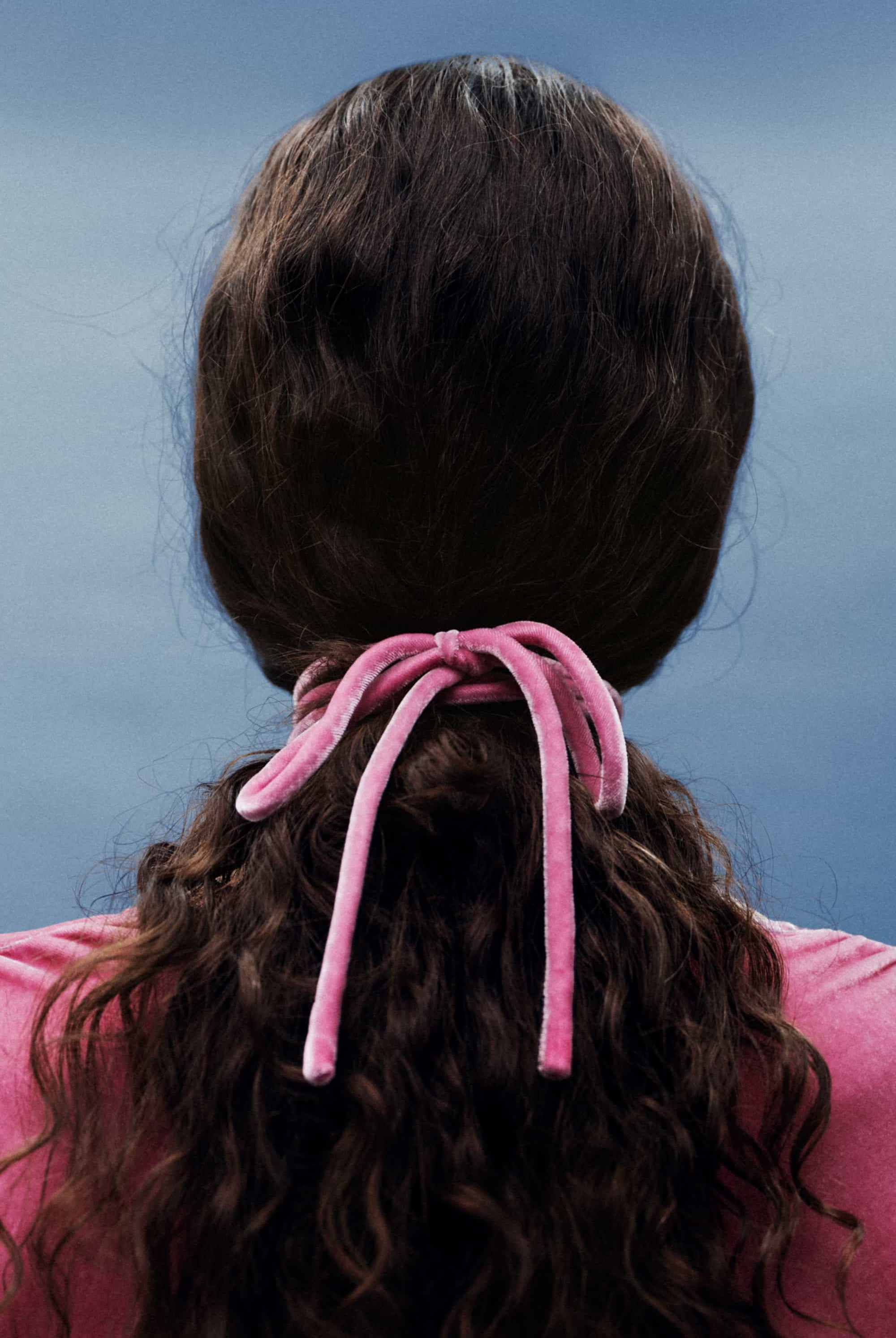 Person with pink hair tie in dark hair against a blue background
