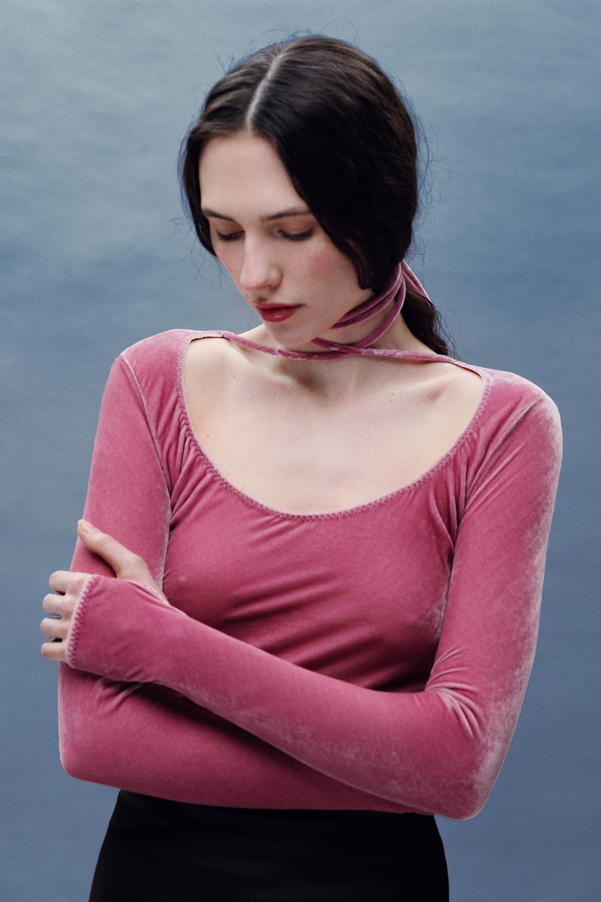 Woman wearing a pink long-sleeve Massima top with a tie detail against a blue background