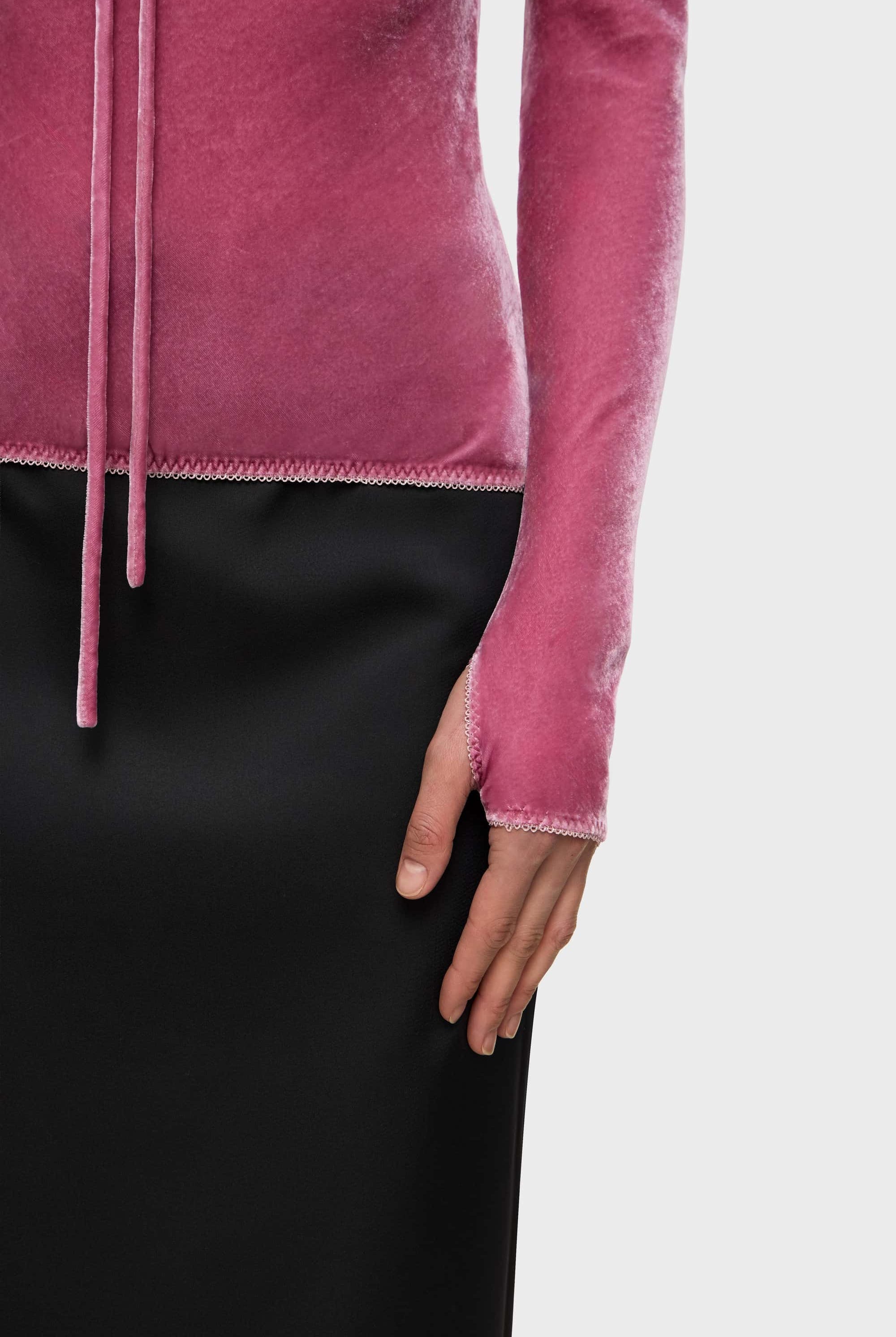 Woman wearing a pink long-sleeve Massima top and black skirt on a white background, details