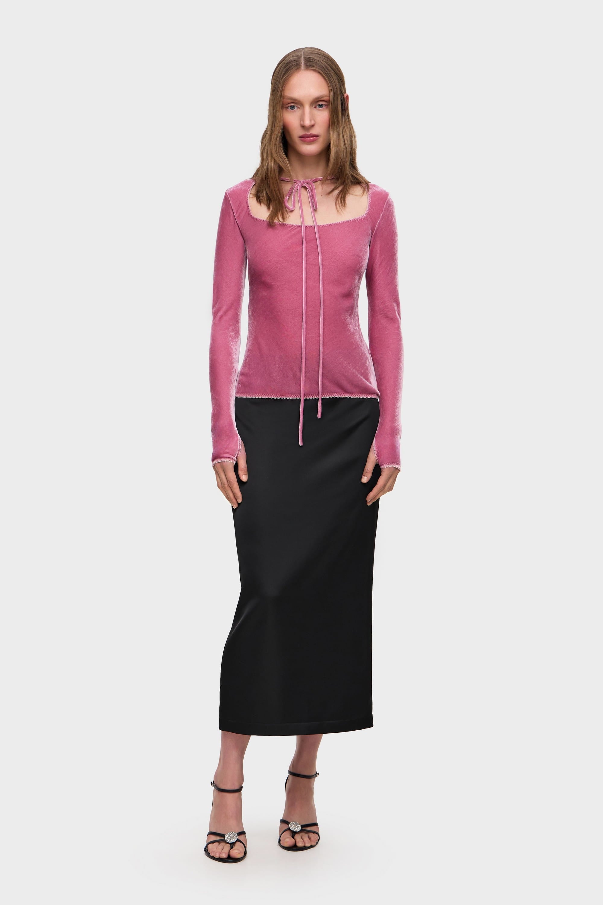 Woman wearing a pink long-sleeve Massima top and black skirt on a white background, front view