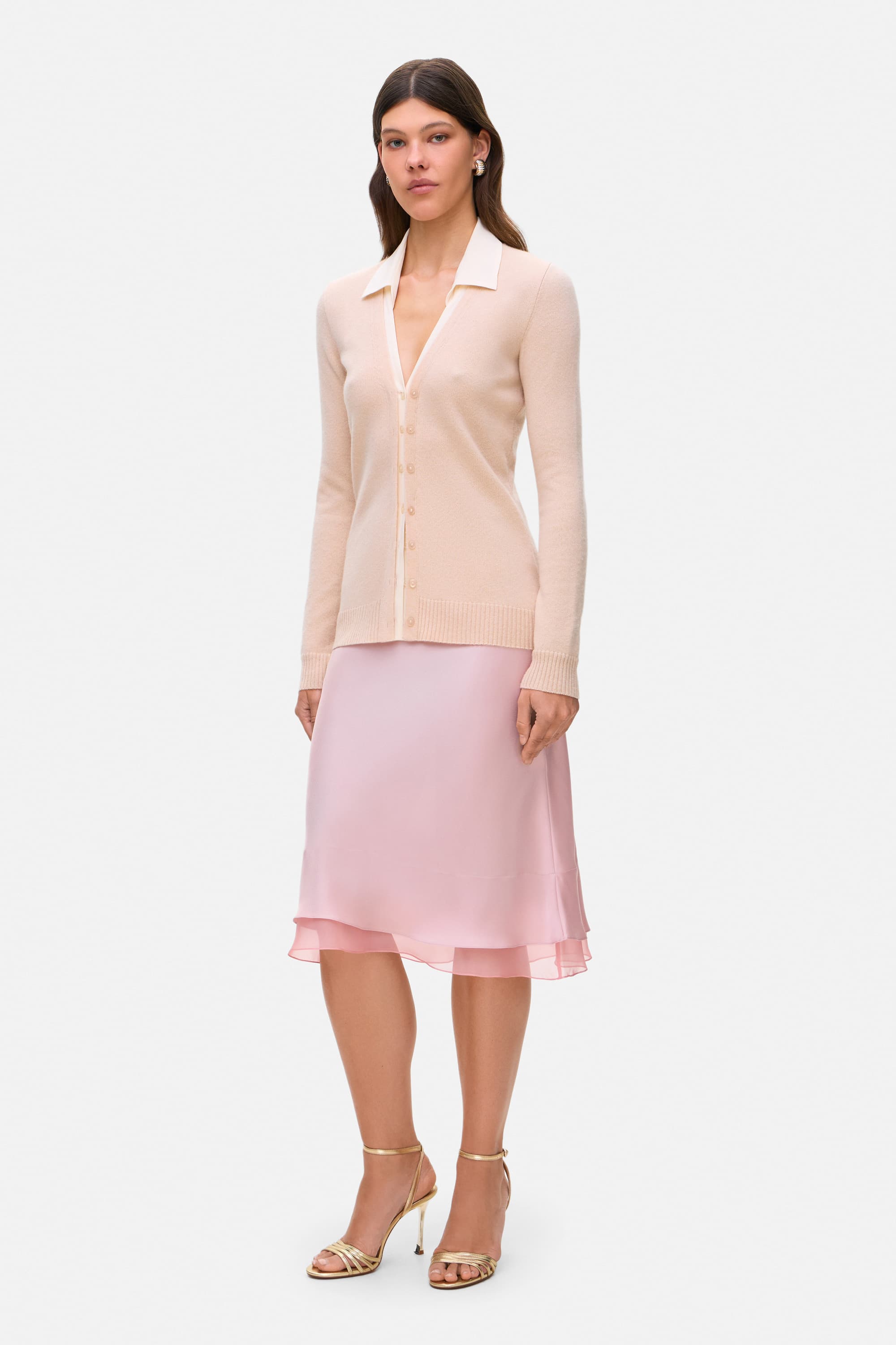 Woman wearing a beige Daniella cardigan and powder pink Elina skirt on a white background, side view