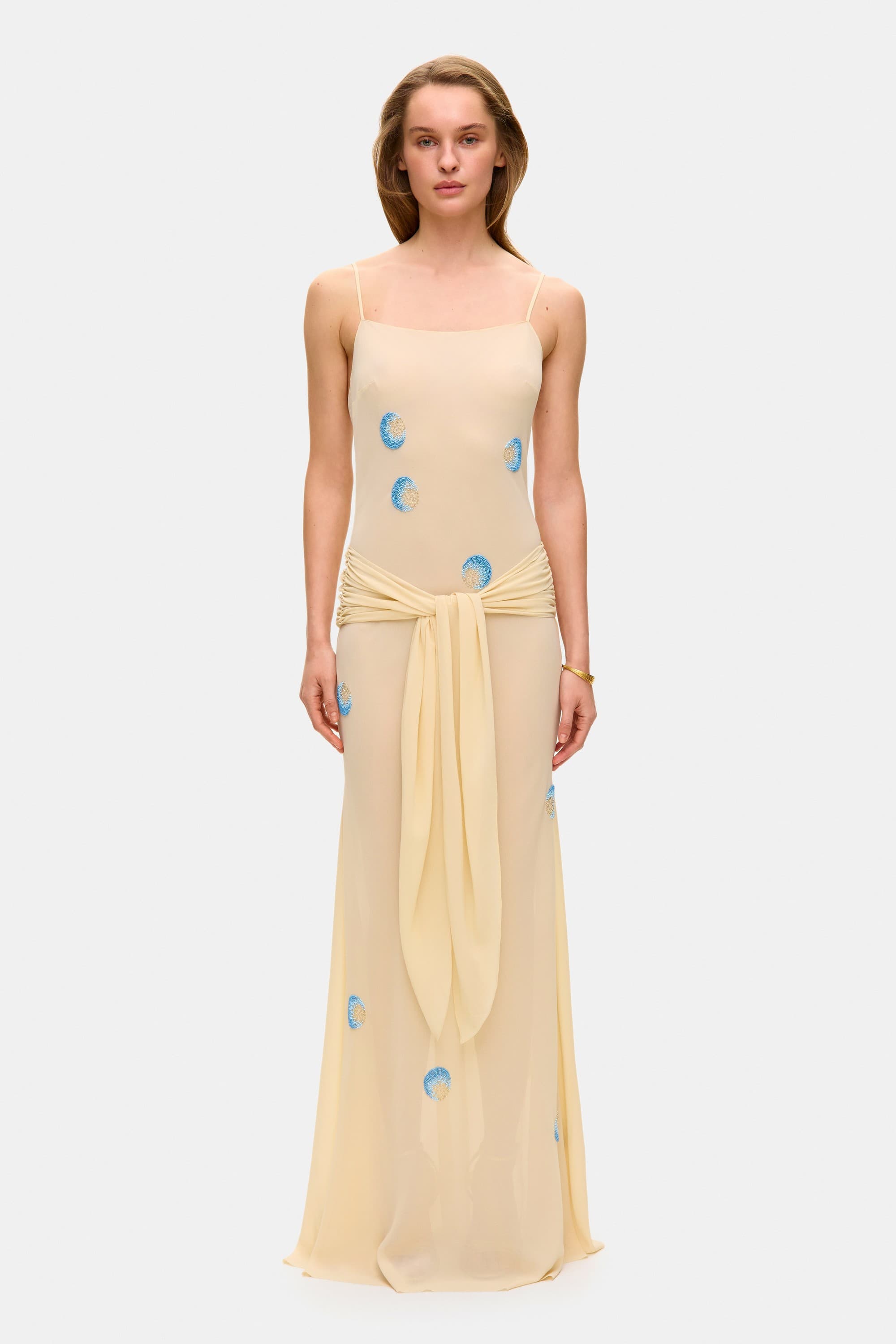 Model in Zoe maxi dress with decorative scarf at the hips, featuring embroidery elements throughout the dress front view