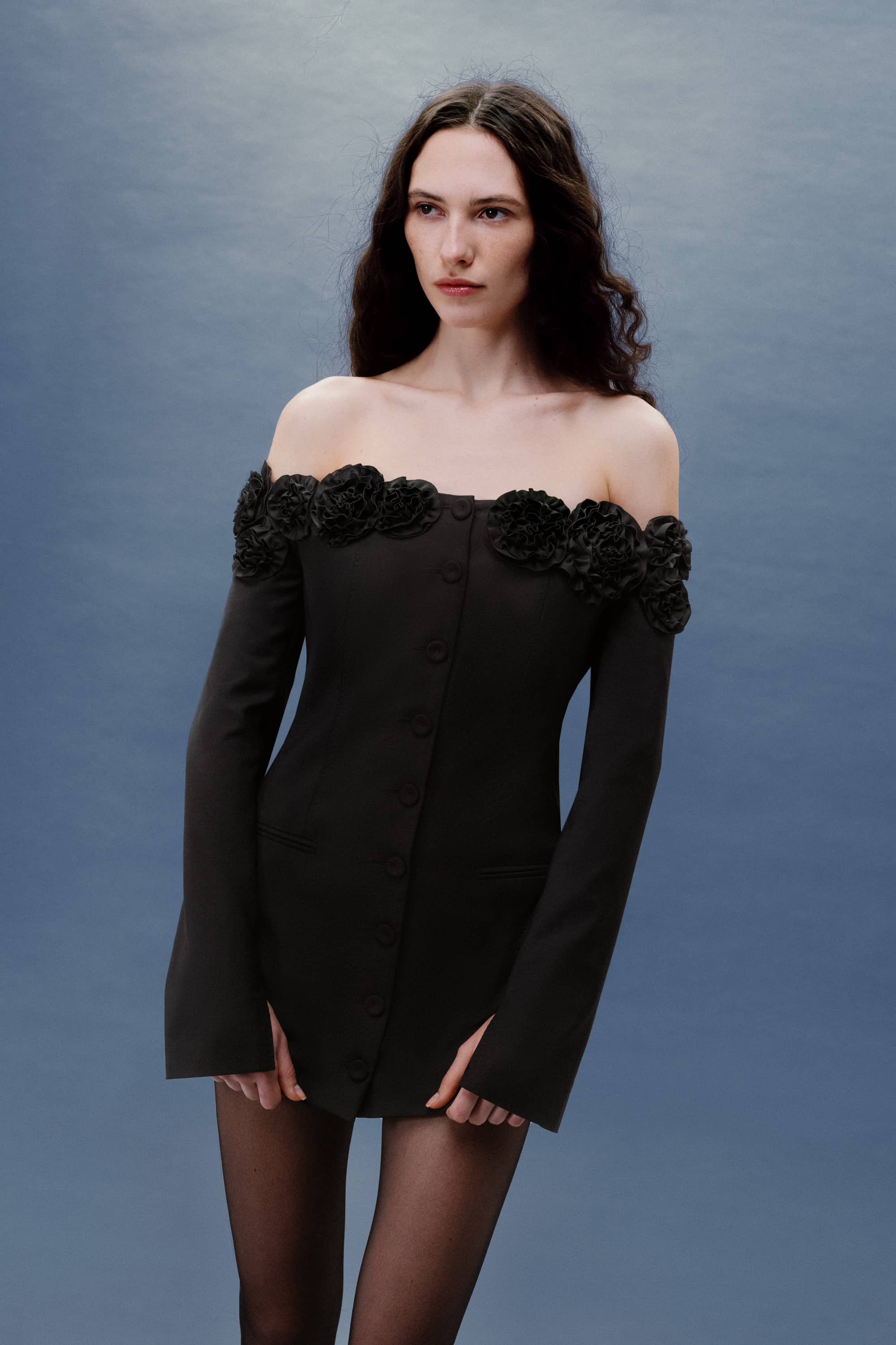 Woman wearing a black off-shoulder Micaela dress with floral details against a gray background