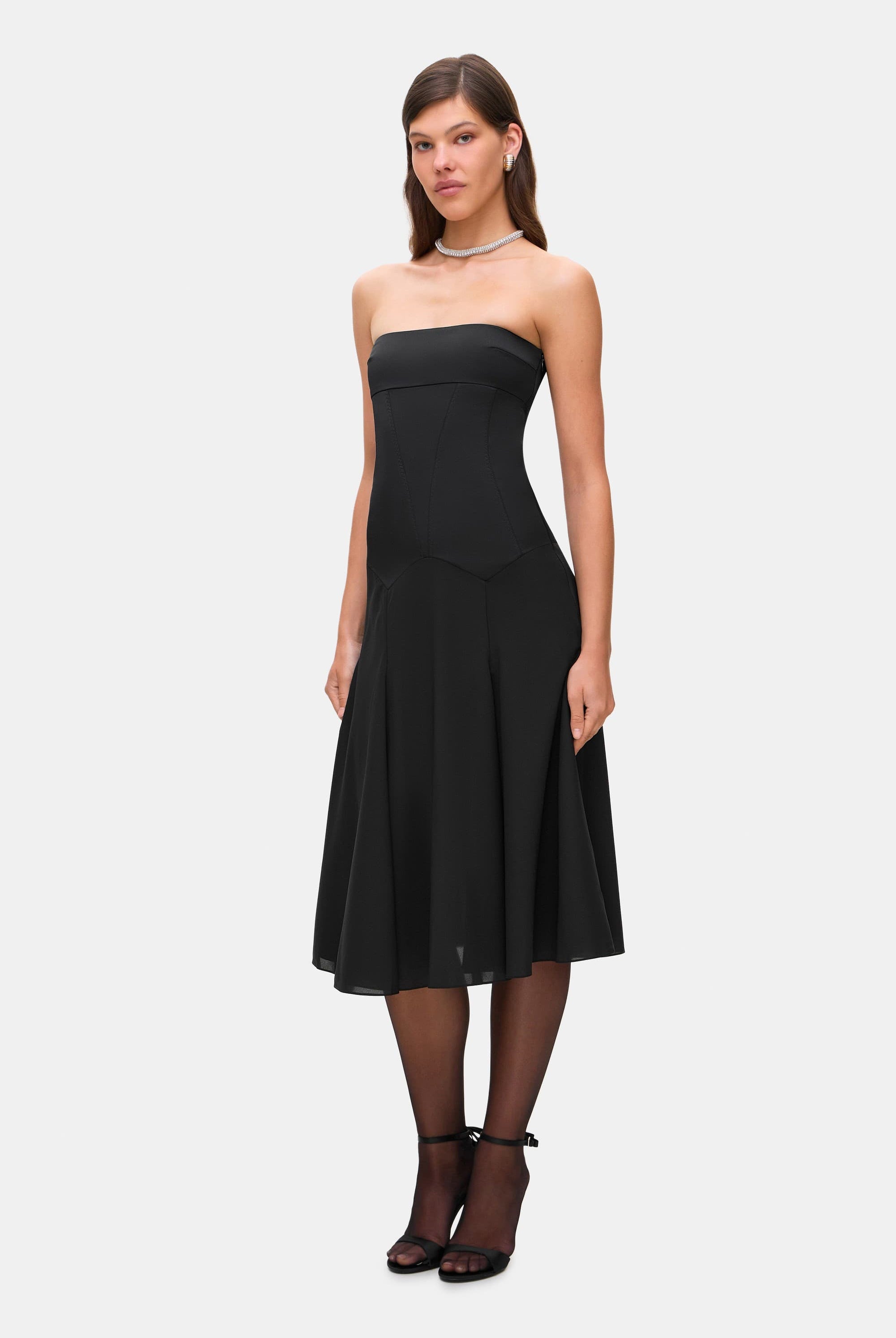 Woman wearing a black strapless Ariella dress on a white background, side view