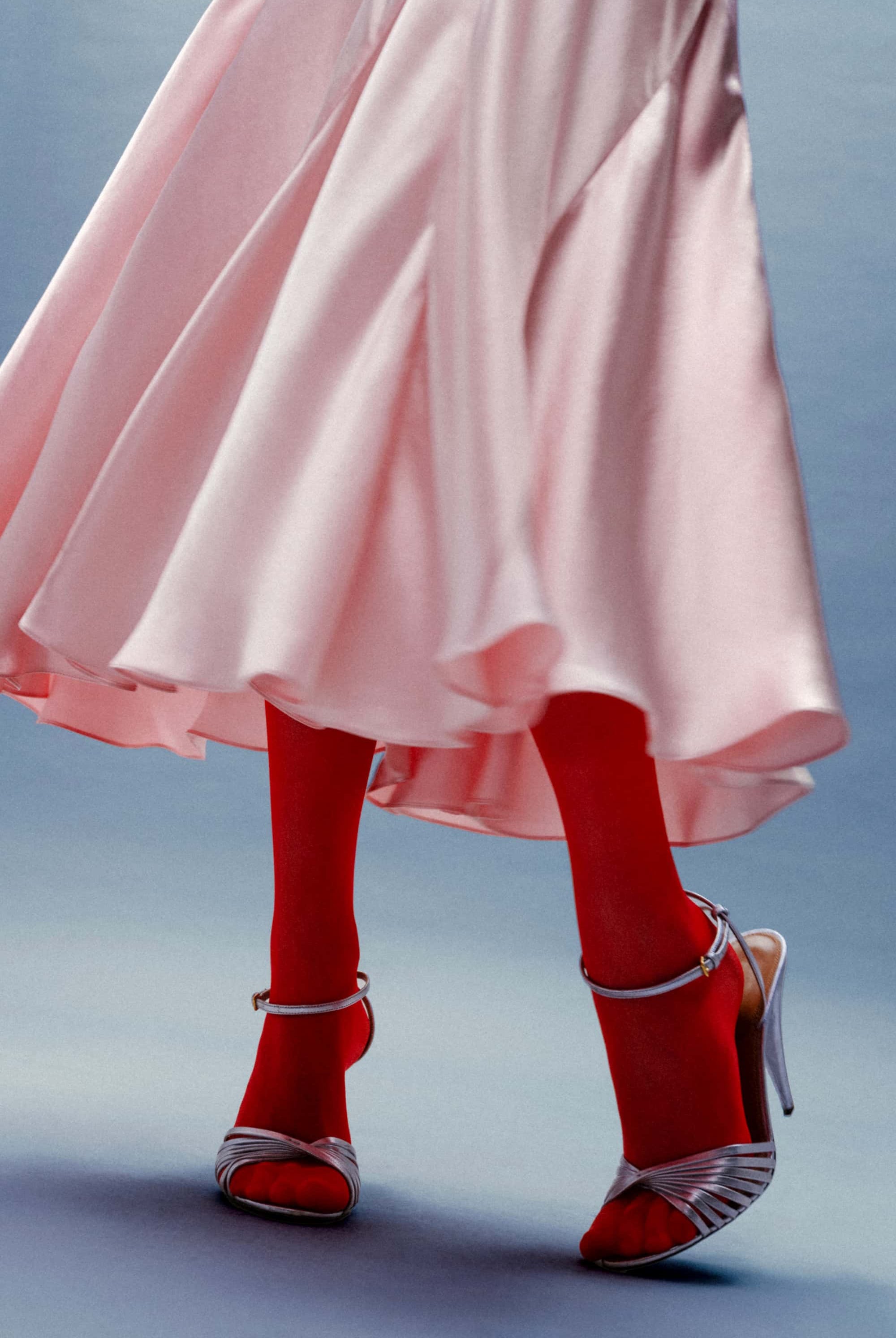 Person wearing a pink Liza dress, red tights, and silver high heels on a light blue background