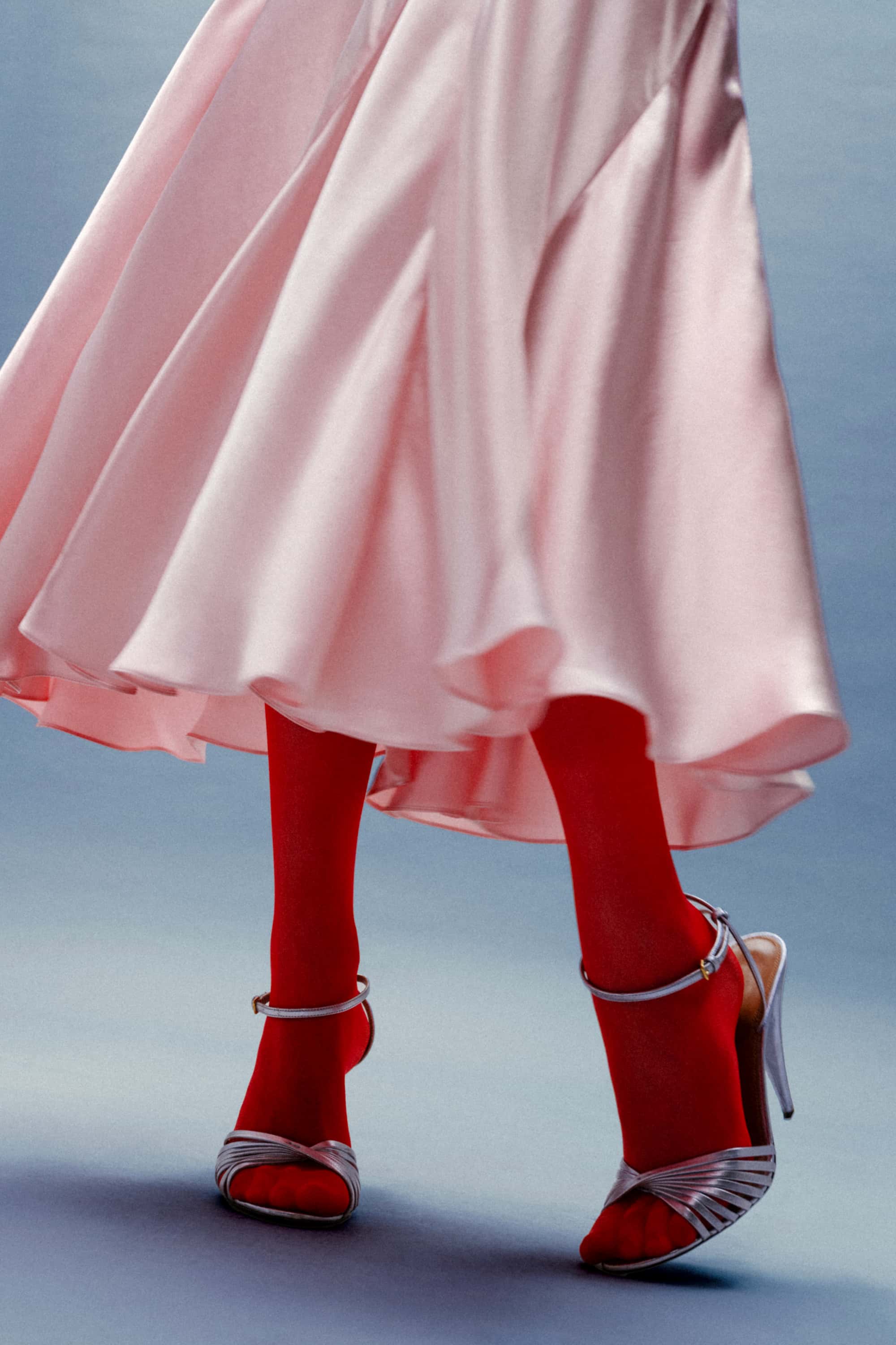 Person wearing a pink Liza dress, red tights, and silver high heels on a light blue background