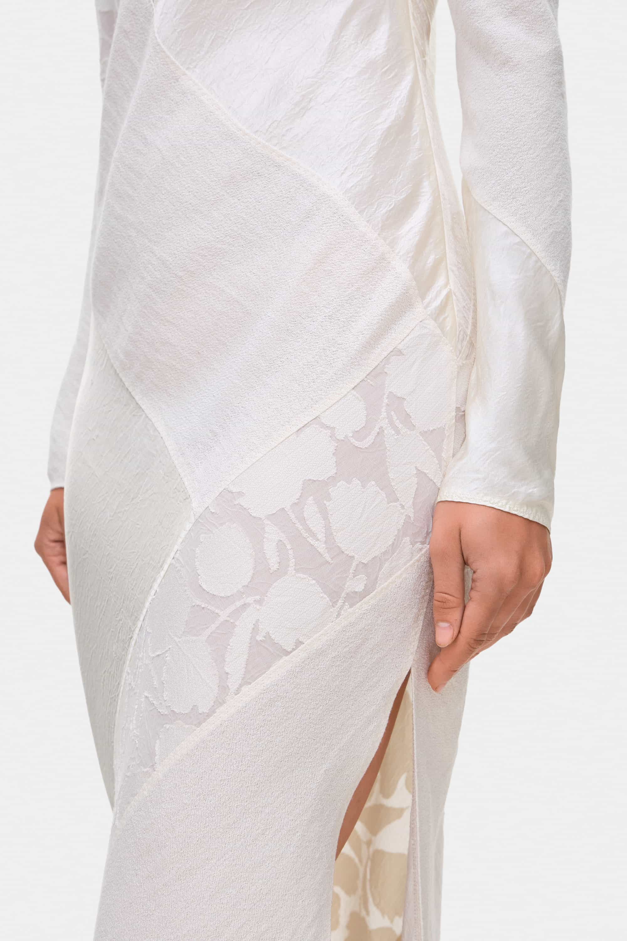 Woman wearing a ivory long-sleeve off-shoulder Santa dress with floral patterns on a white background, side details view