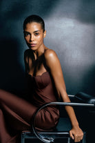 Woman in a brown Tulip dress sitting on a chair against a dark background