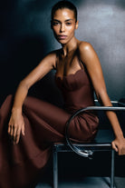 Woman in a brown Tulip dress sitting on a chair against a dark background