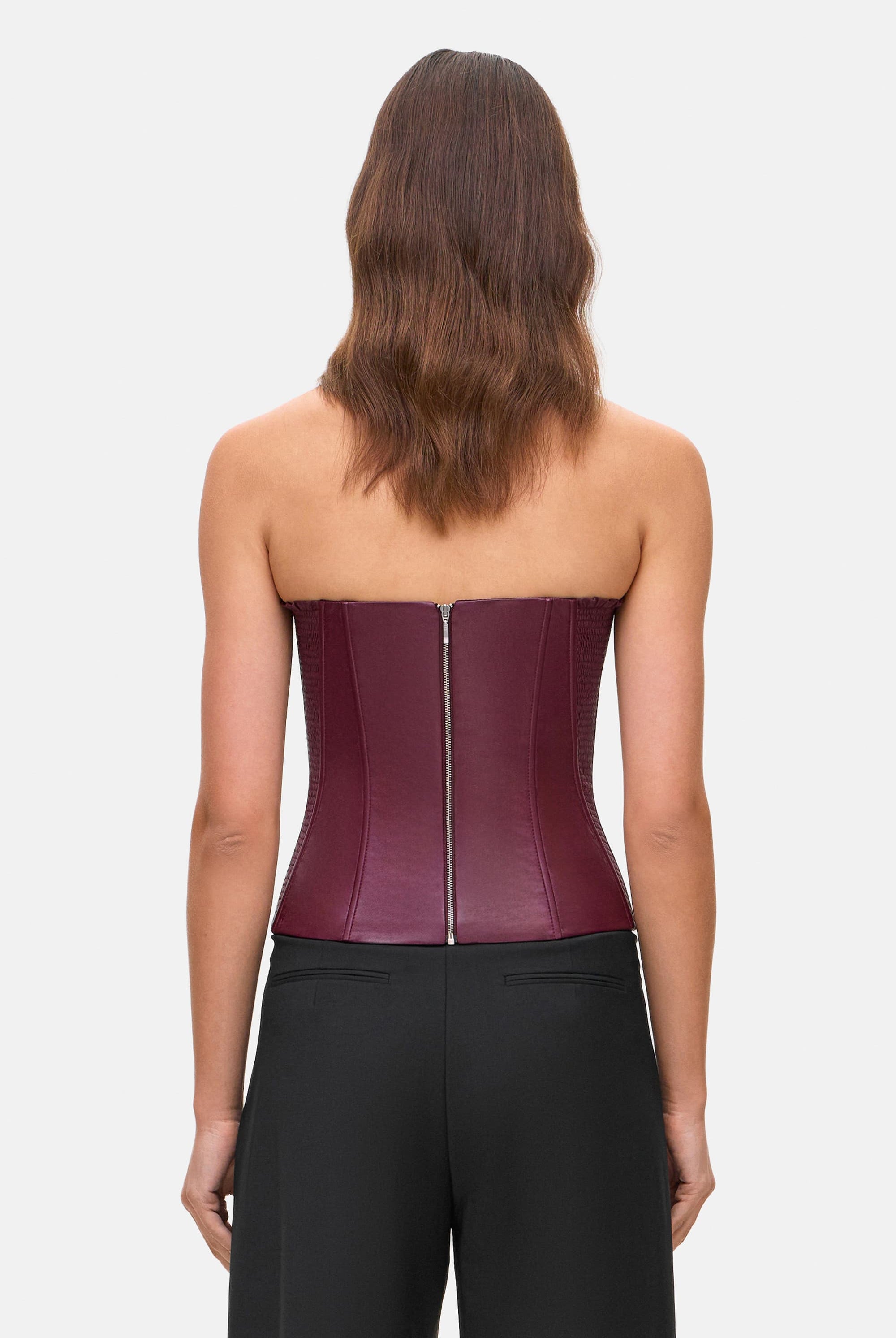 Woman wearing a strapless burgundy Susana corset and black pants on a white background, back view
