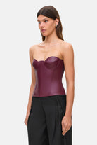 Woman wearing a strapless burgundy Susana corset and black pants on a white background, side view