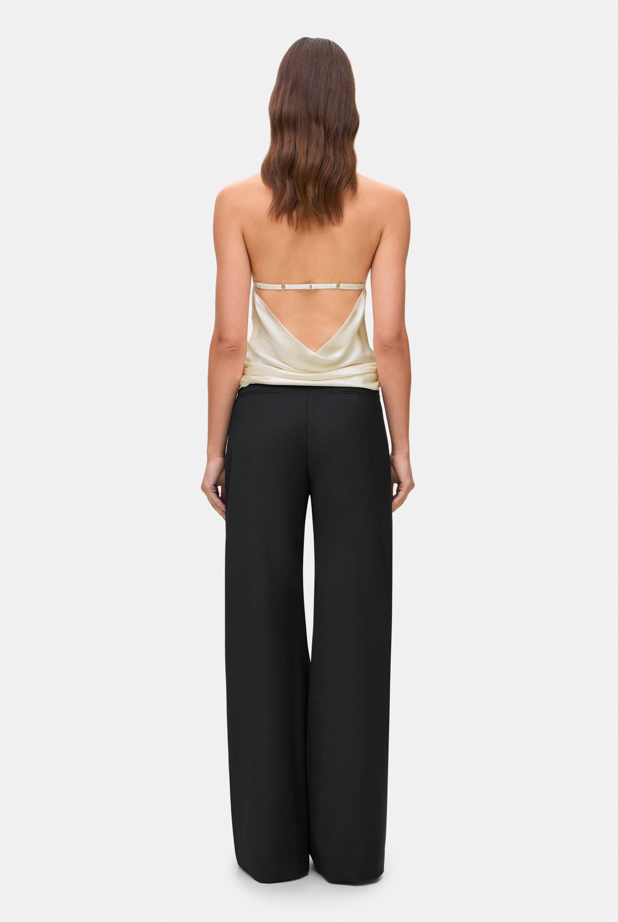 Woman wearing a ivory sleeveless Soma top and black wide-leg pants, back view