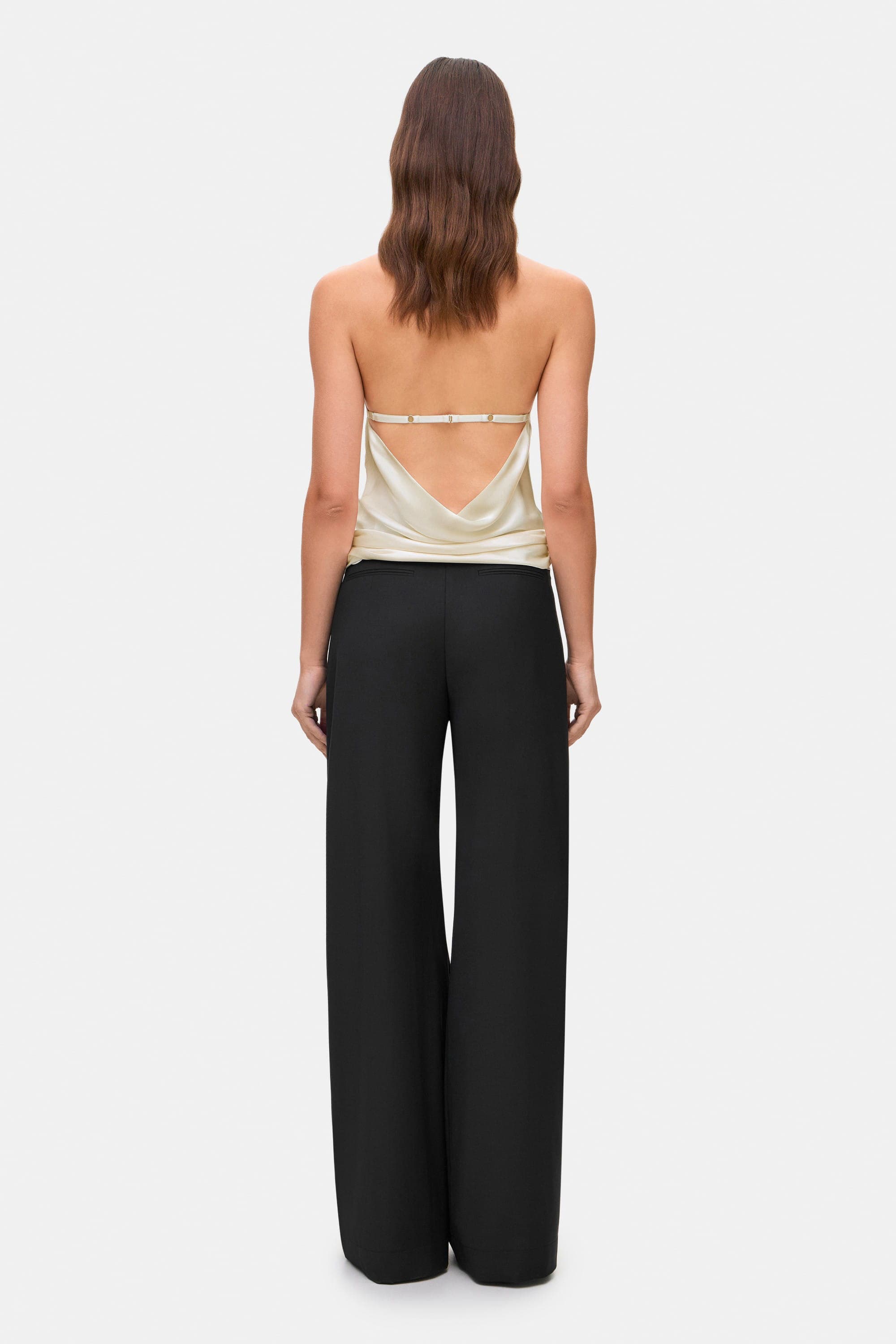Woman wearing a ivory sleeveless Soma top and black wide-leg pants, back view