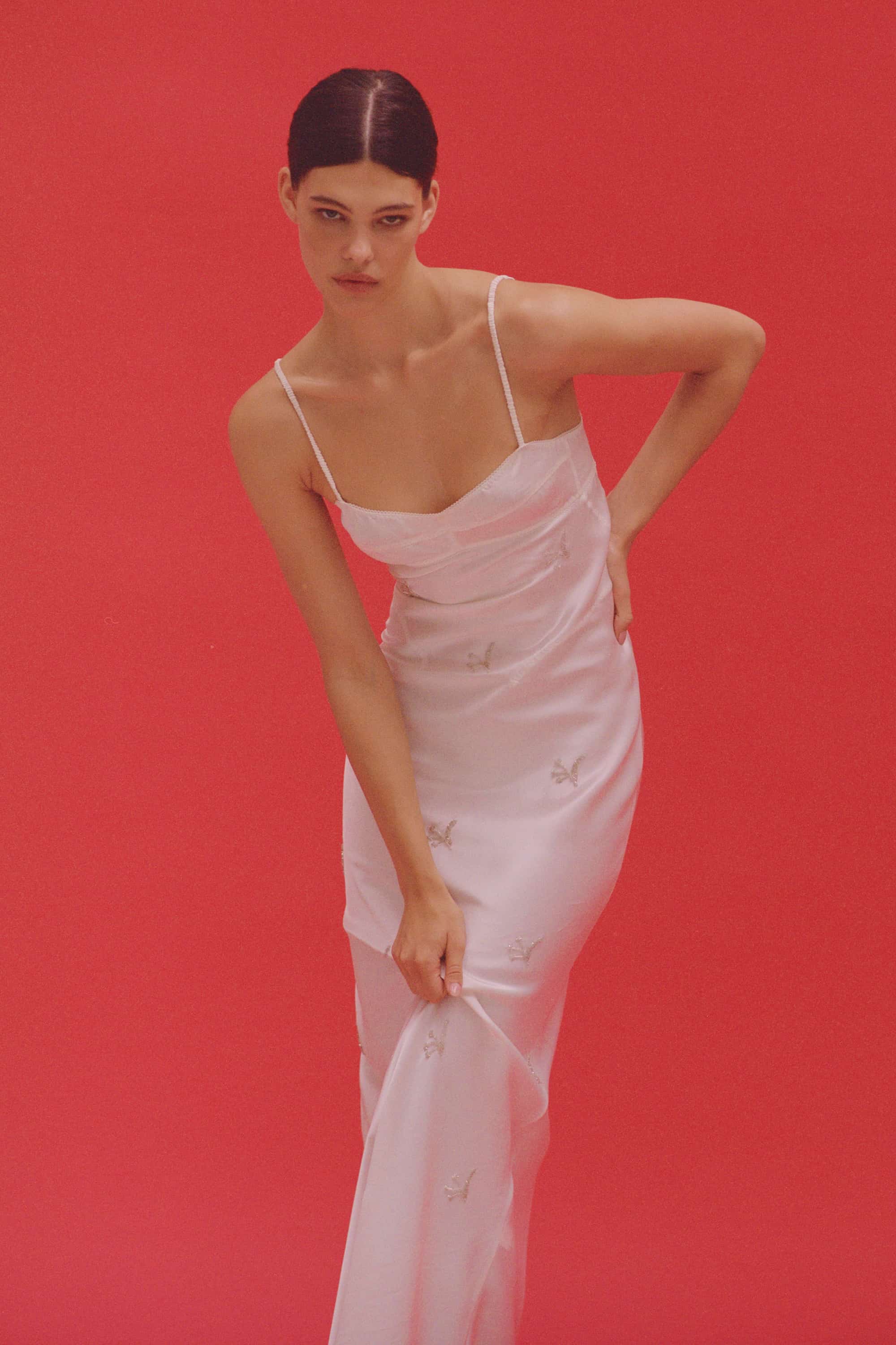 Woman wearing bustier style bodice Beaded Waterlily maxi dress with embroidery against a red background