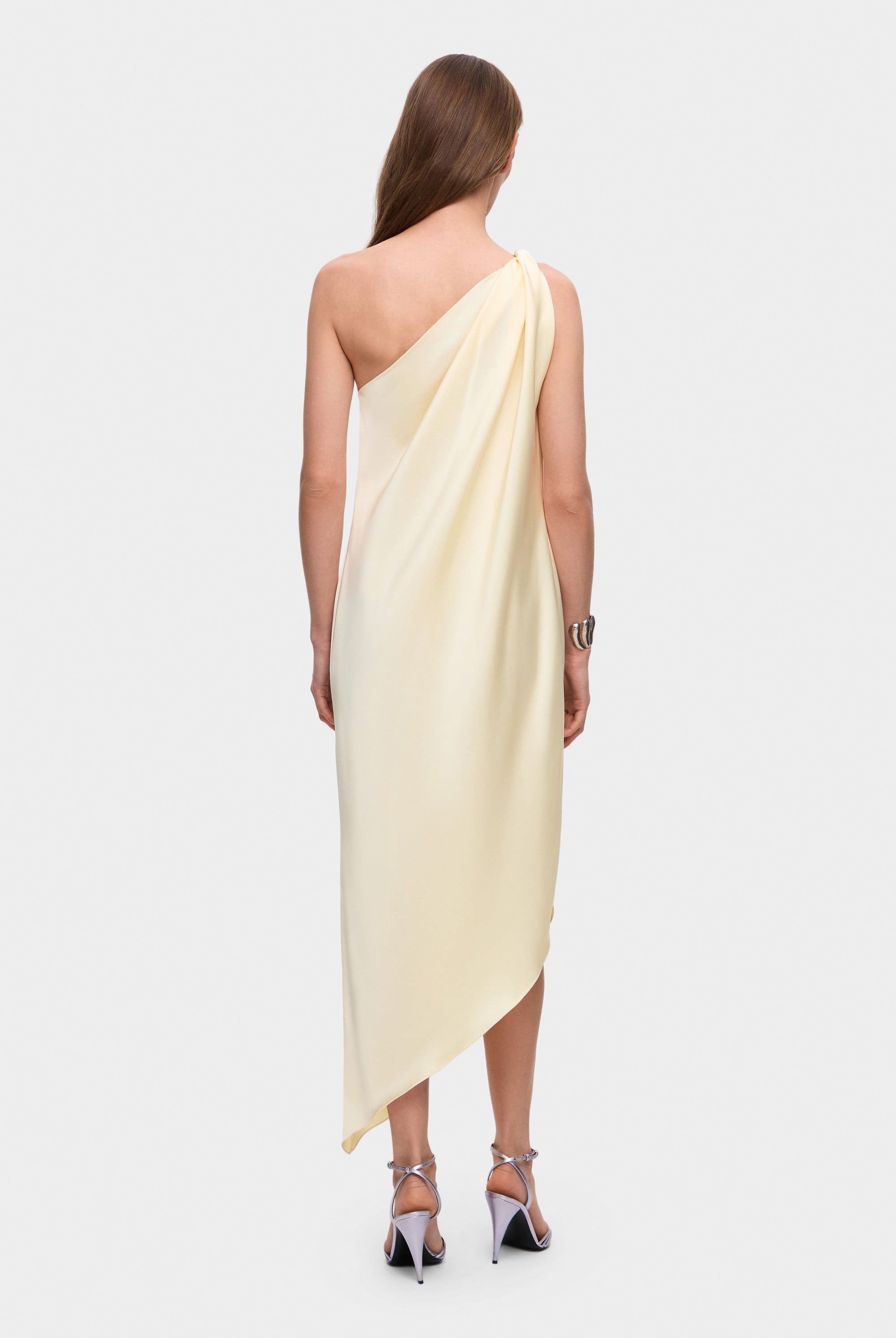 Woman wearing a one-shoulder buttermilk Rina dress on a white background, back view