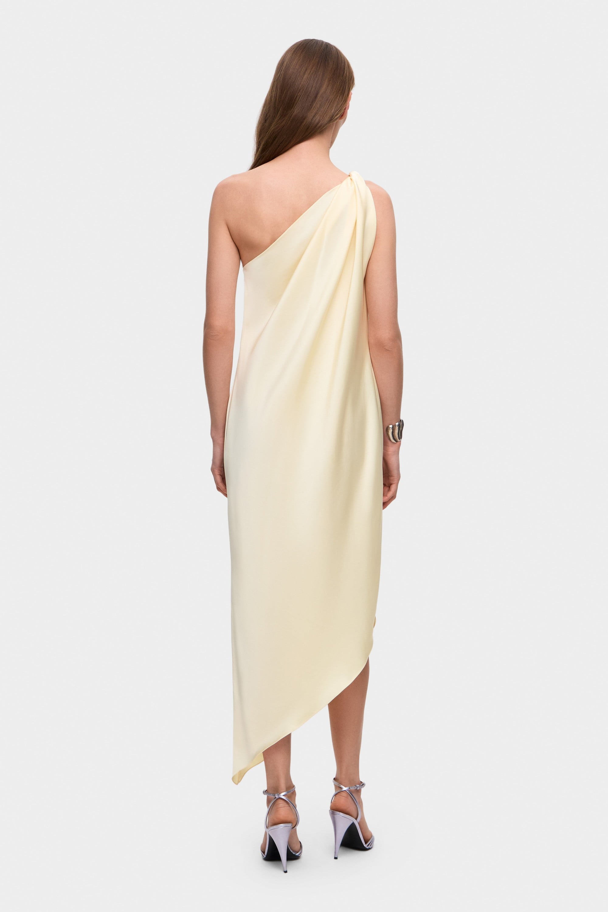 Woman wearing a one-shoulder buttermilk Rina dress on a white background, back view