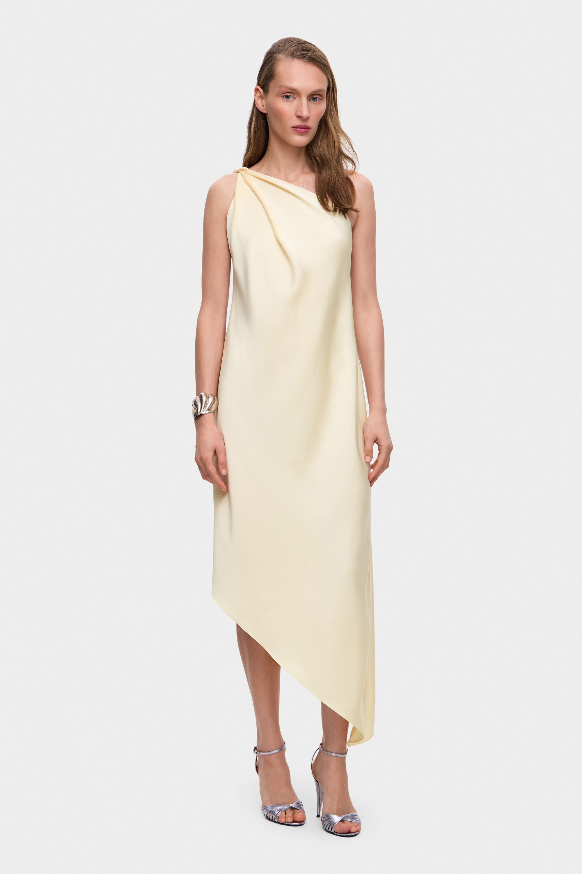Woman wearing a one-shoulder buttermilk Rina dress on a white background, front view