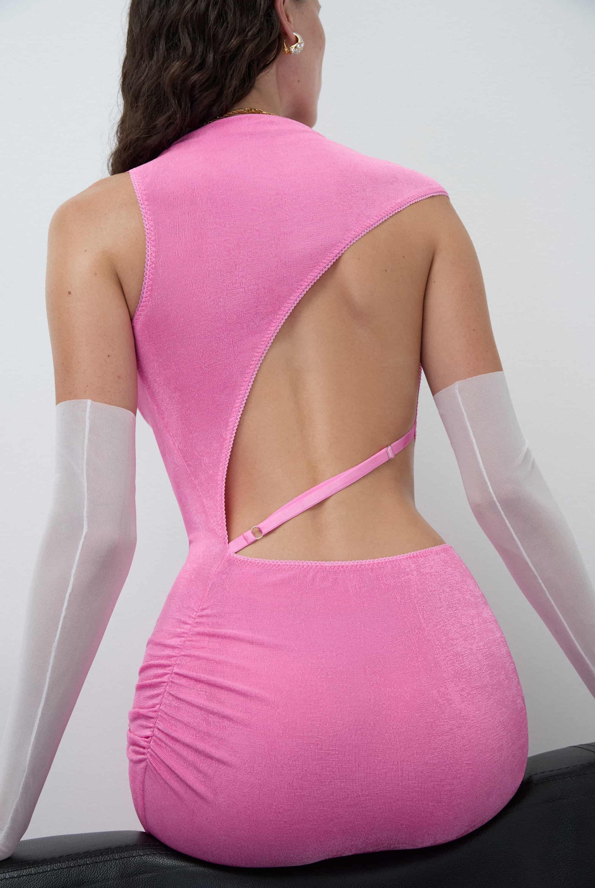 Woman wearing a pink sleeveless Aya dress with cut-out design on a white background, detail back view