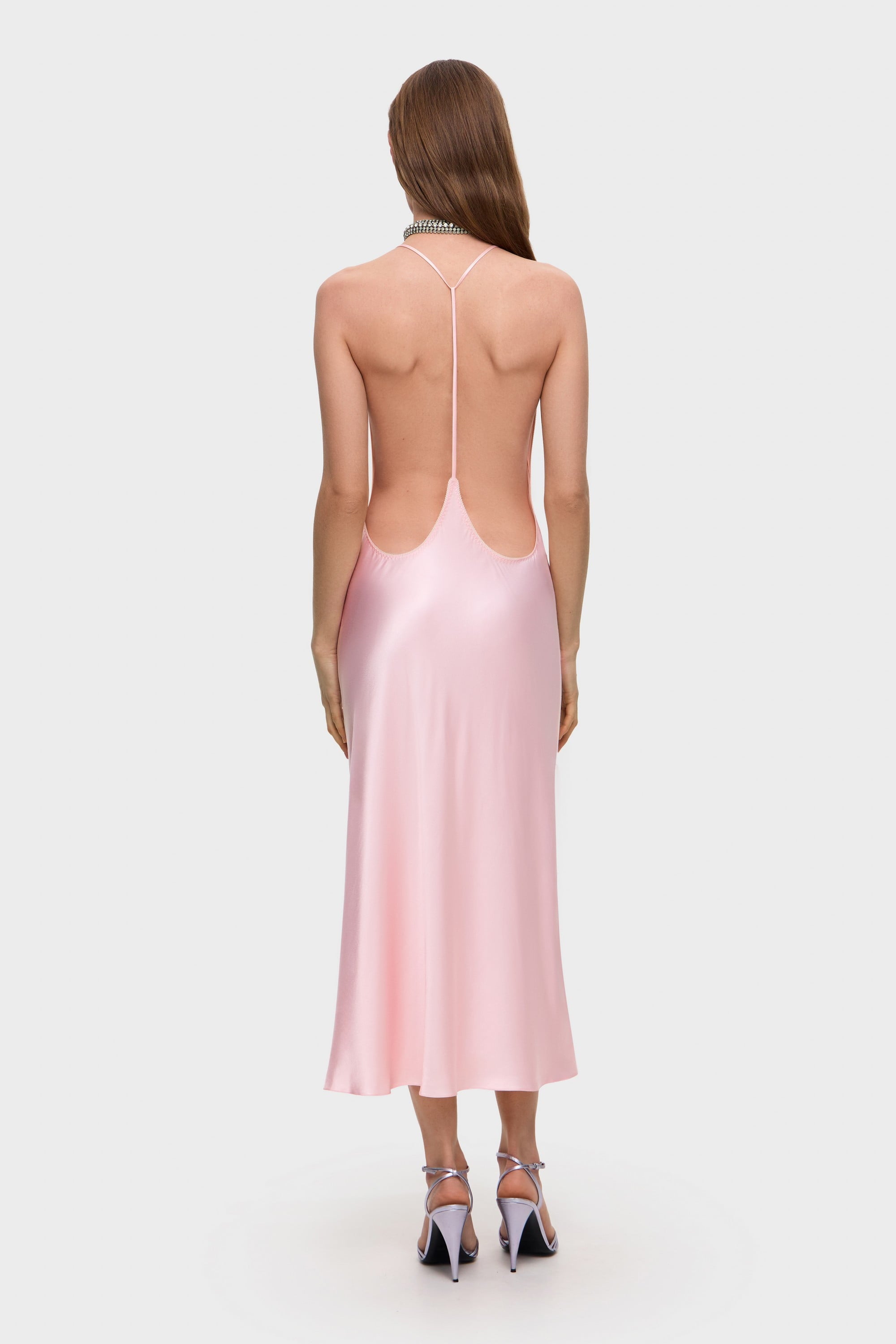 Woman wearing a light pink Justina midi dress with thin straps on a white background, back view