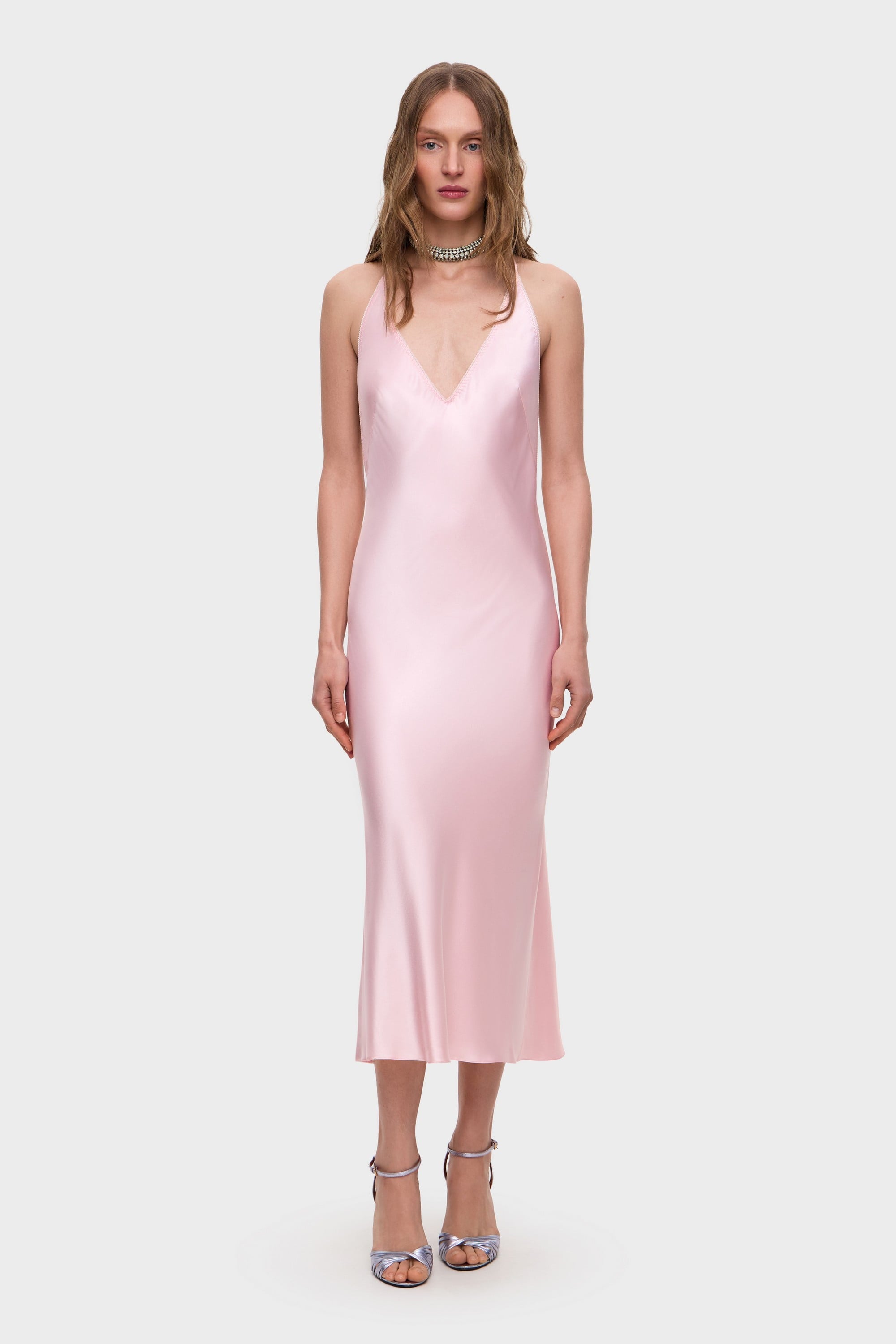 Woman wearing a light pink Justina midi dress with thin straps on a white background, front view