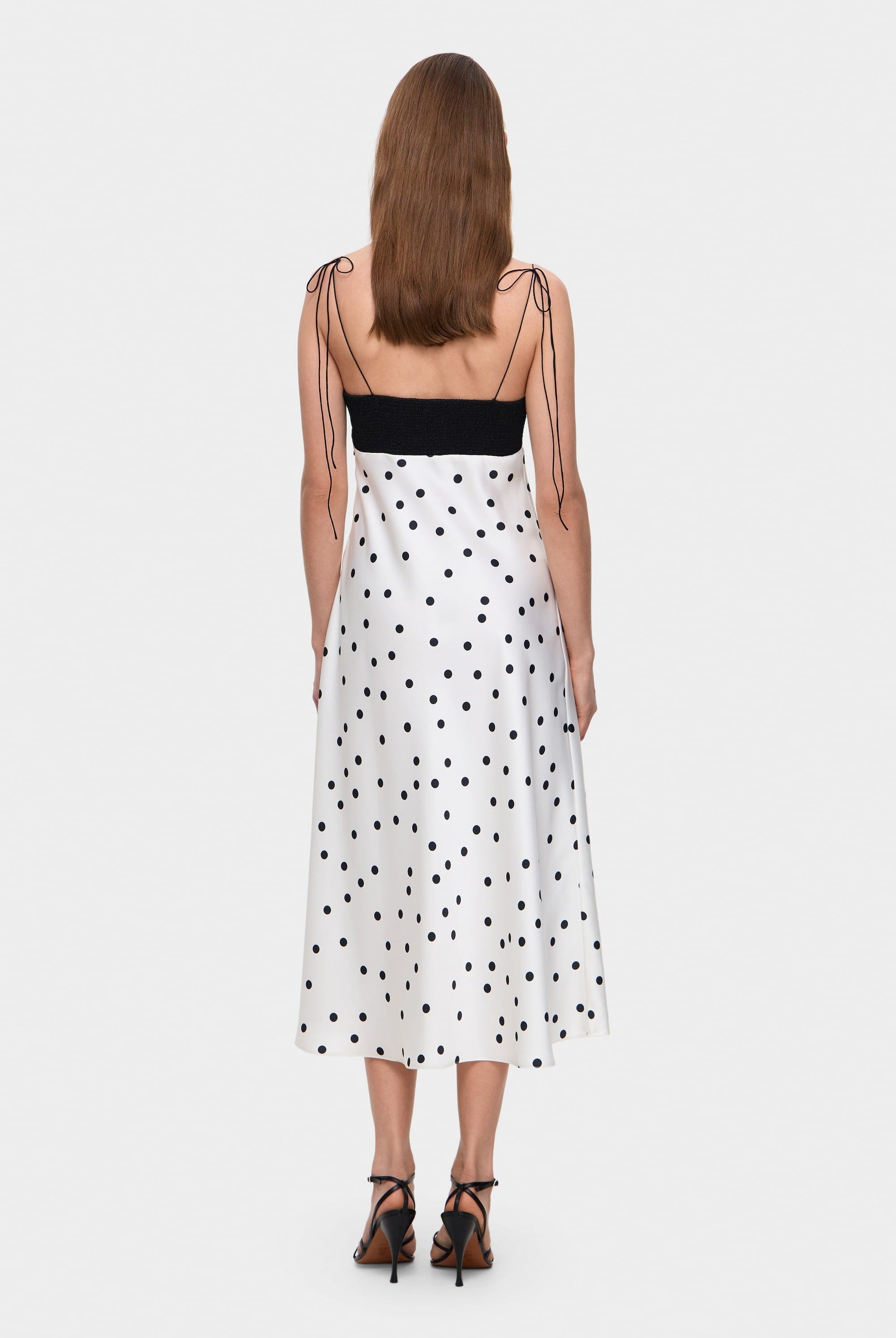 Woman wearing a black and white polka dot Erika dress with thin straps on a white background, back view