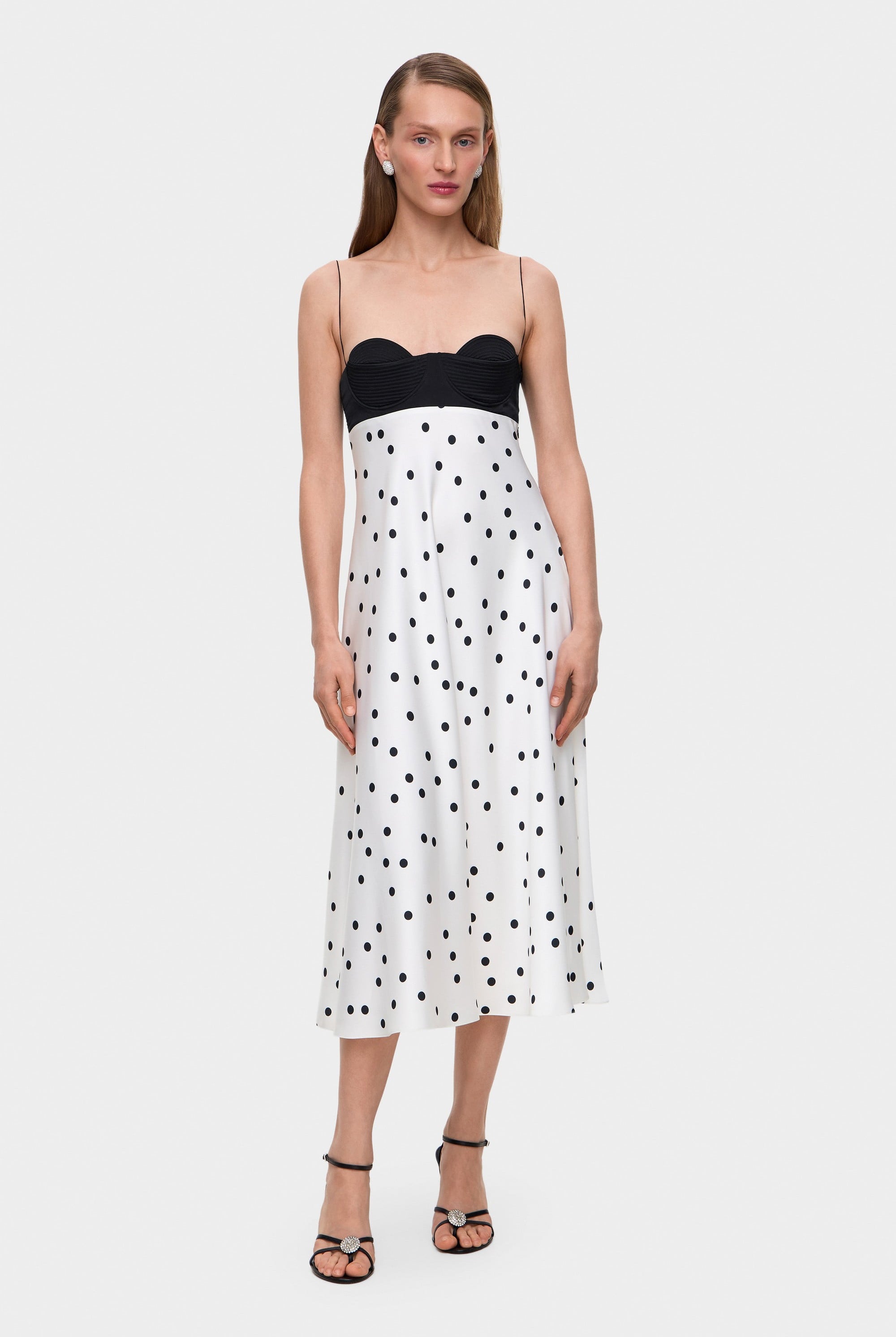 Woman wearing a black and white polka dot Erika dress with thin straps on a white background, front view