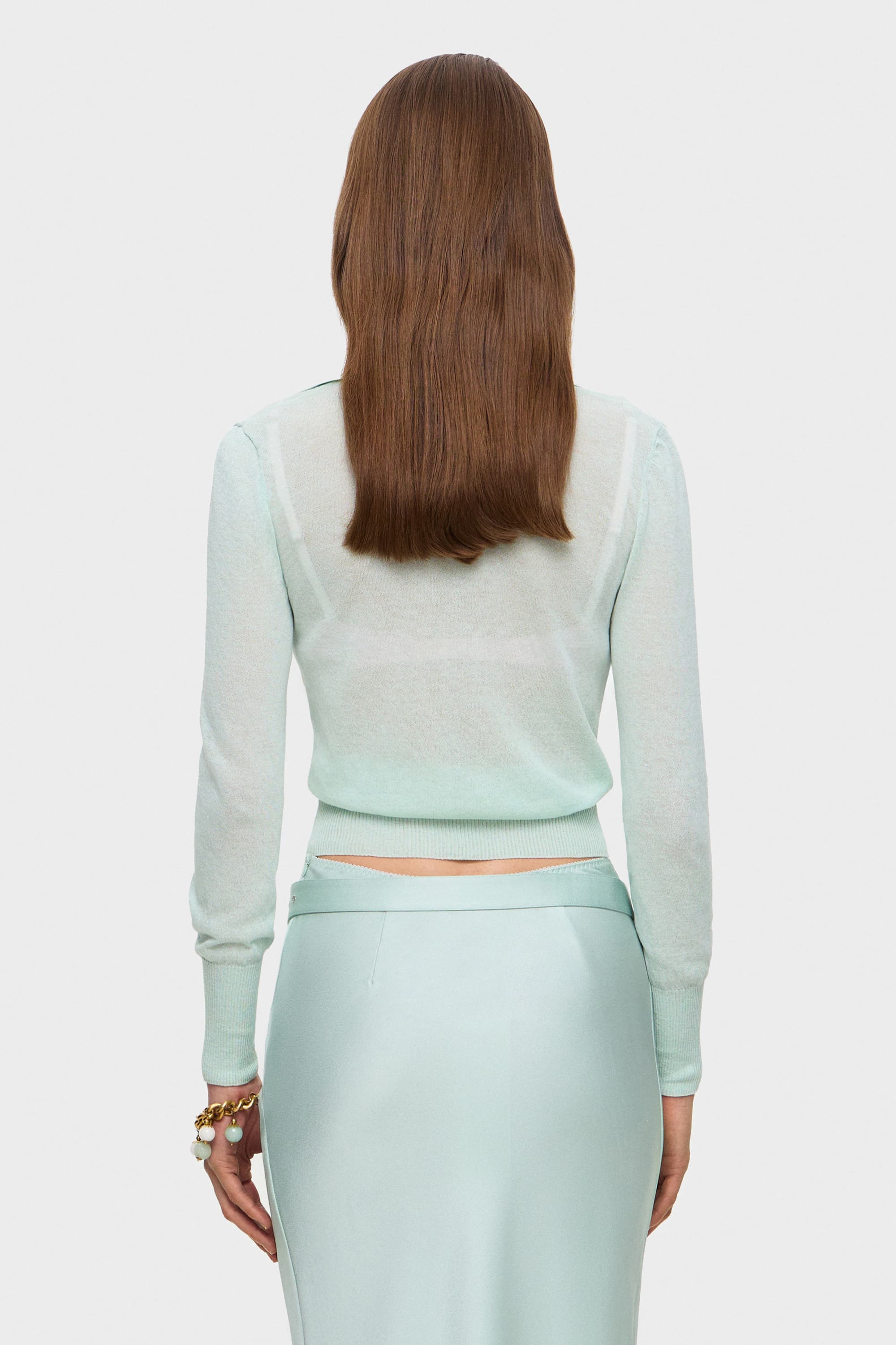 Woman wearing a light mint Ensley cardigan over a pink bra on a white background, back view