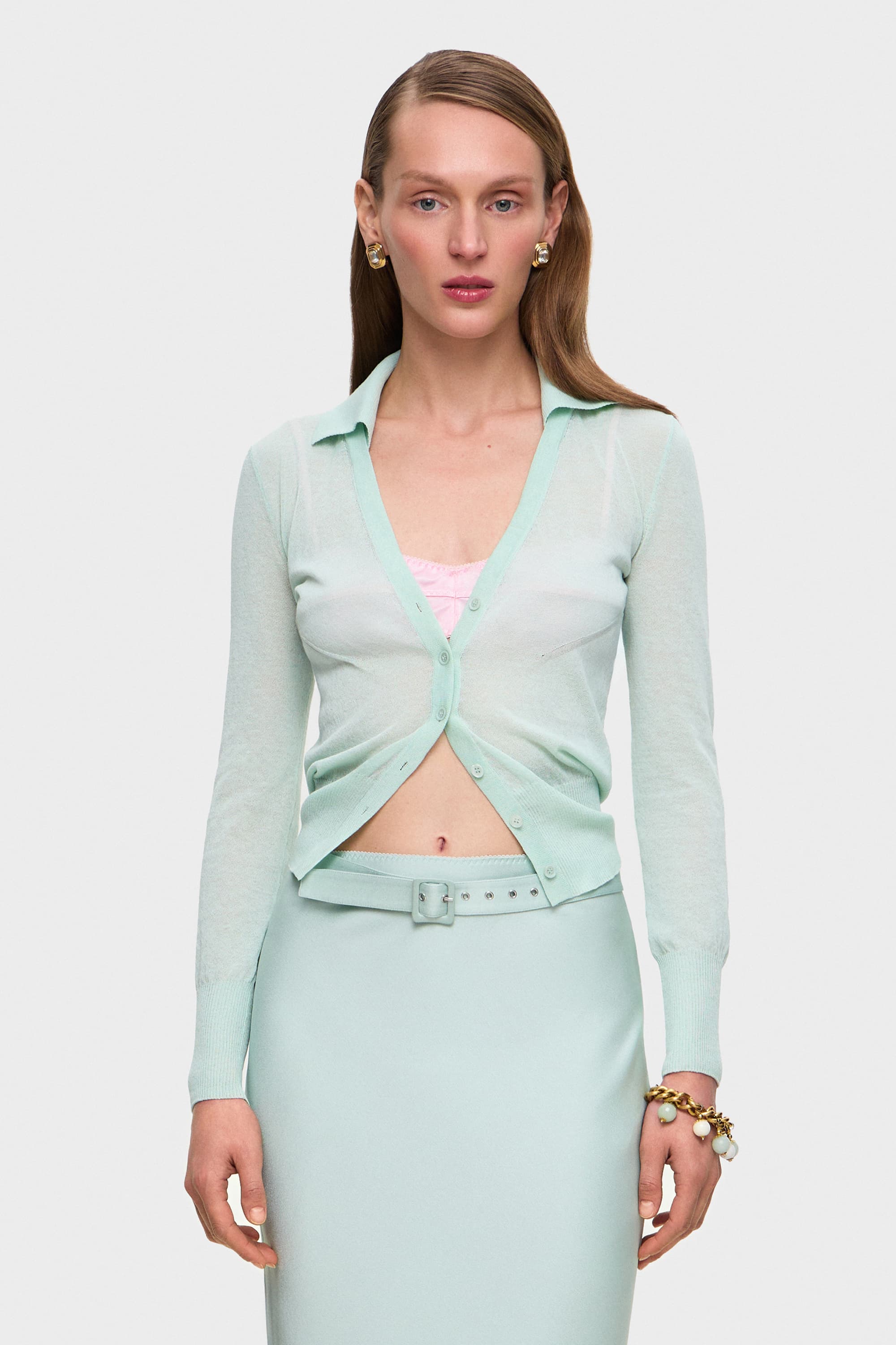 Woman wearing a light mint Ensley cardigan over a pink bra on a white background, front view