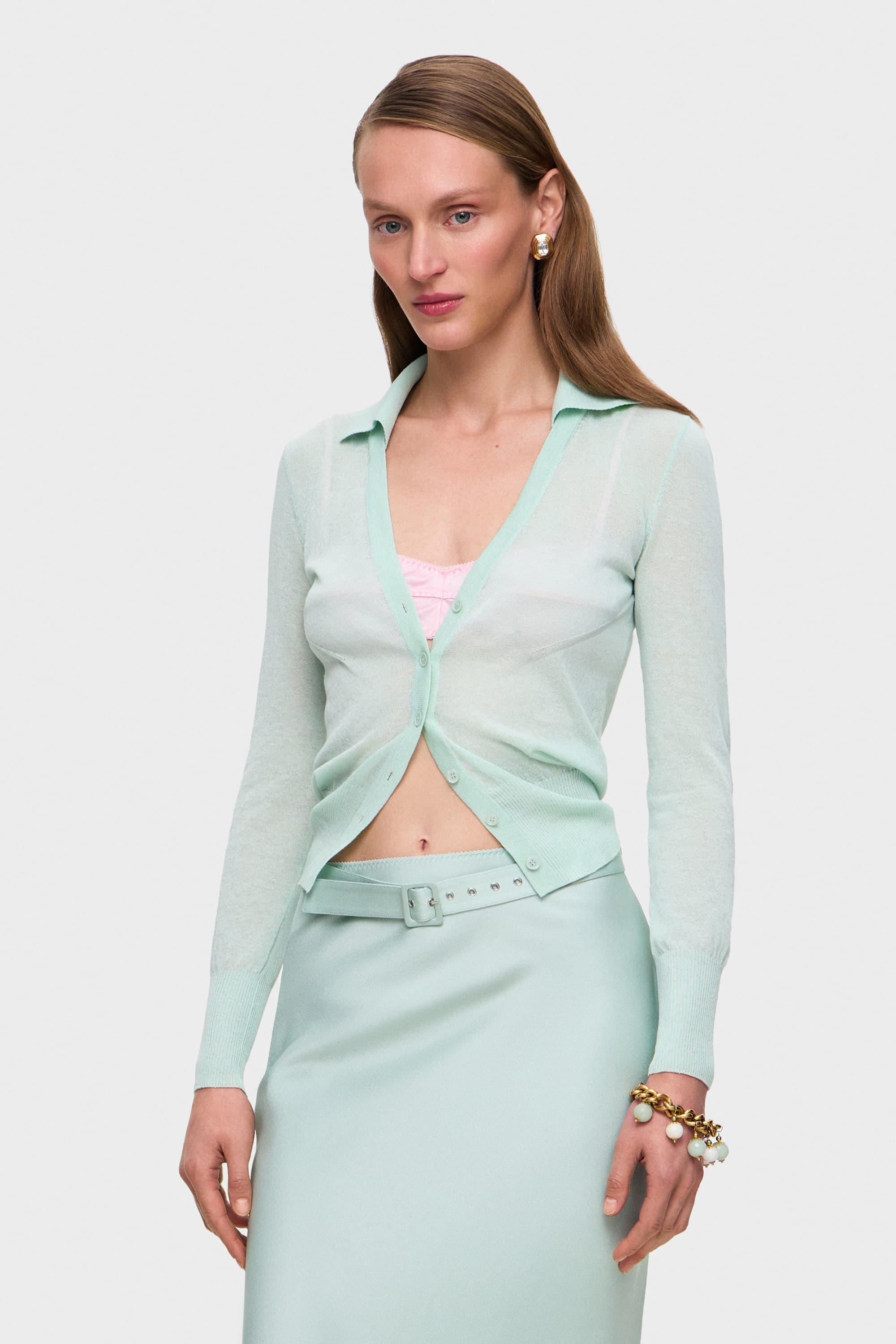 Woman wearing a light mint Ensley cardigan over a pink bra on a white background, side view