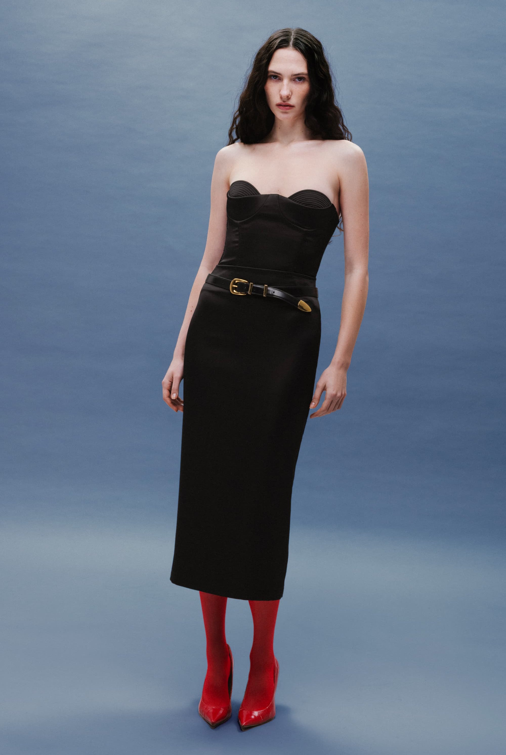 Woman wearing a black Kaya skirt with belt and red shoes against a gray background