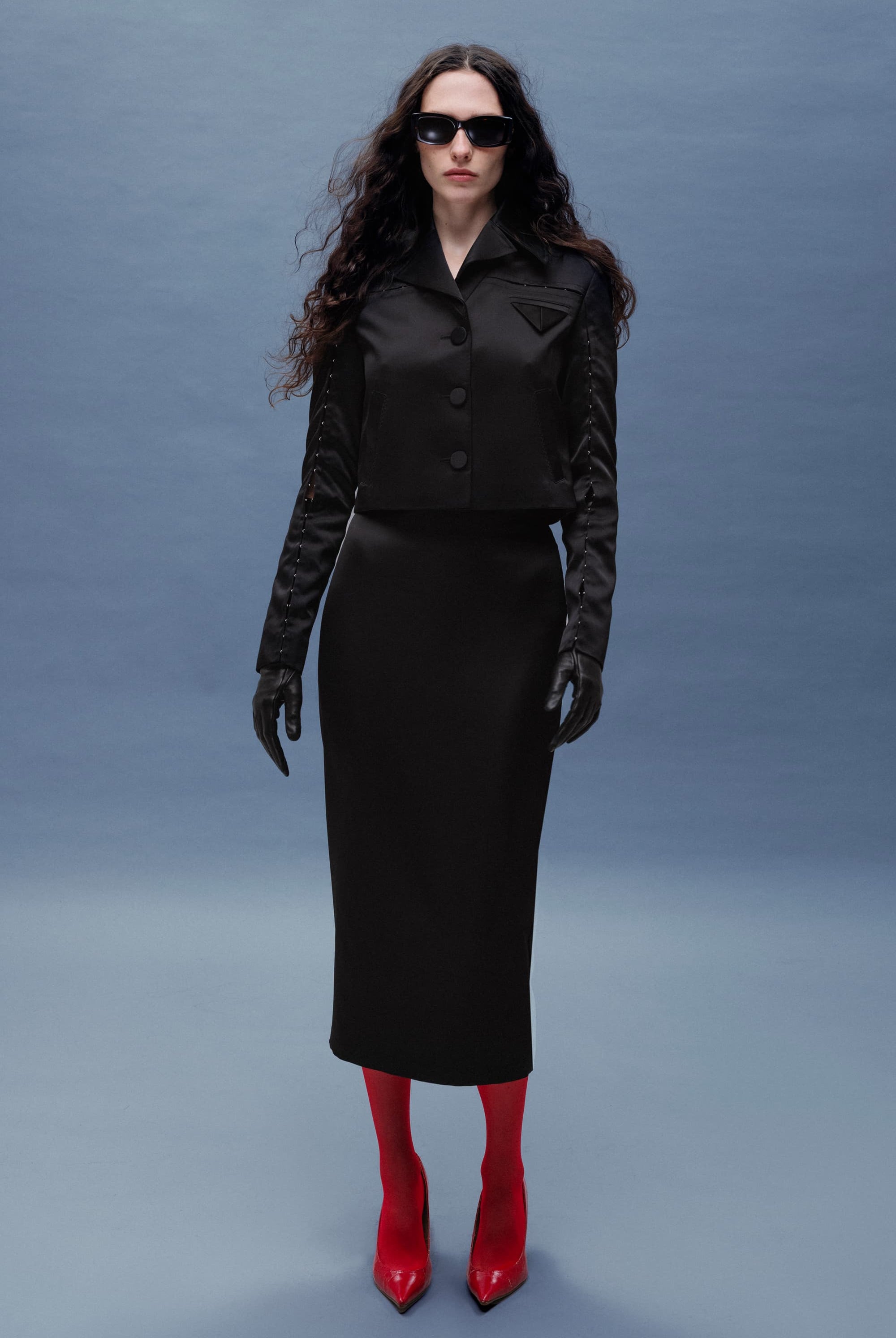 Woman wearing a black Kaya skirt with red shoes against a gray background