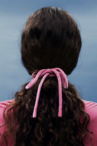 Person with pink hair tie in dark hair against a blue background