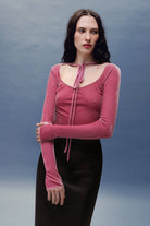 Woman wearing a pink long-sleeve Massima top with a tie detail against a blue background