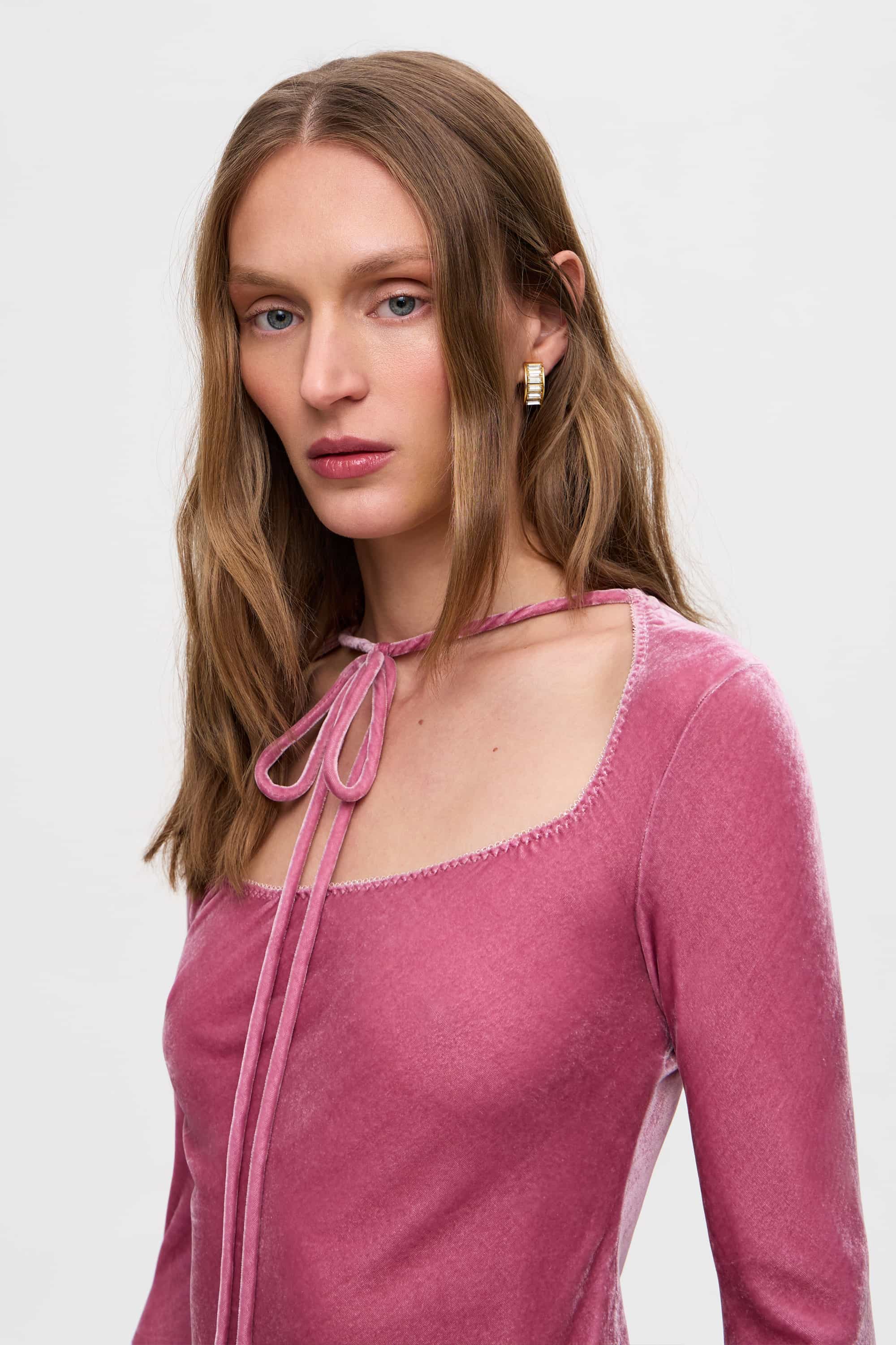 Woman wearing a pink long-sleeve Massima top on a white background, details side view