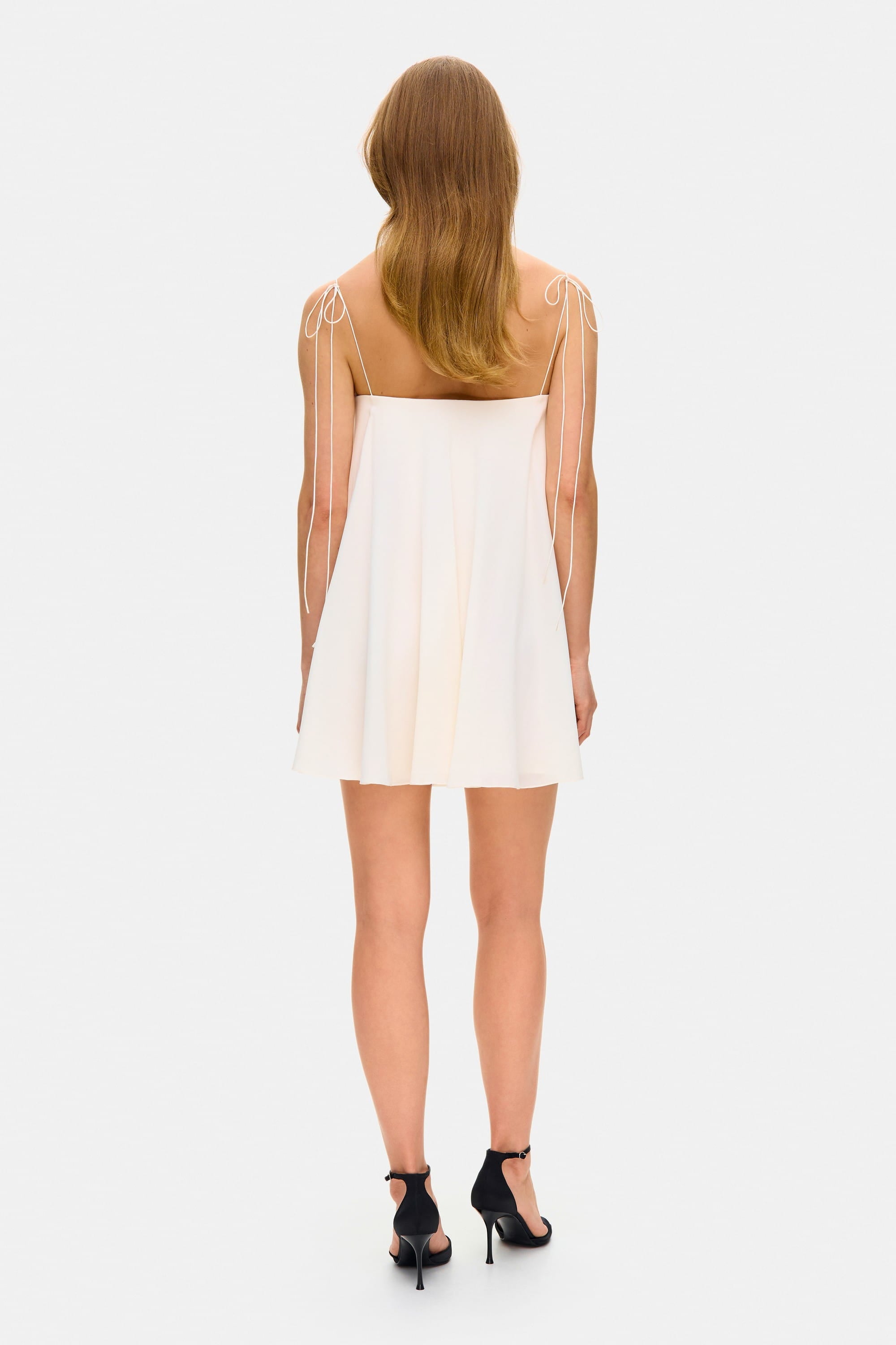 Model in loose Tonia mini dress with tulip-shaped decorated cups and straps tied into bows back view