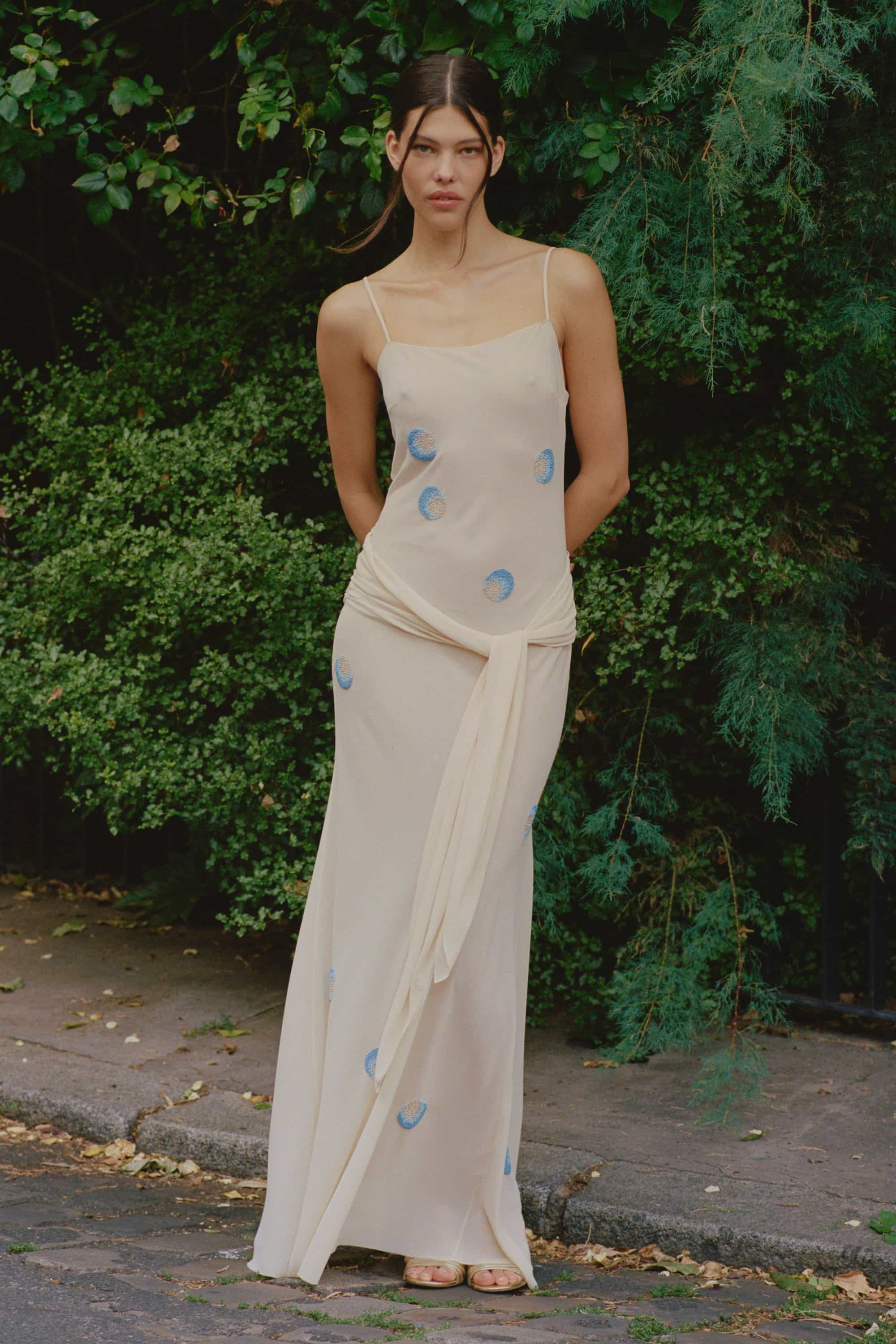 Model in Zoe maxi dress with decorative scarf at the hips, featuring embroidery elements throughout the dress
