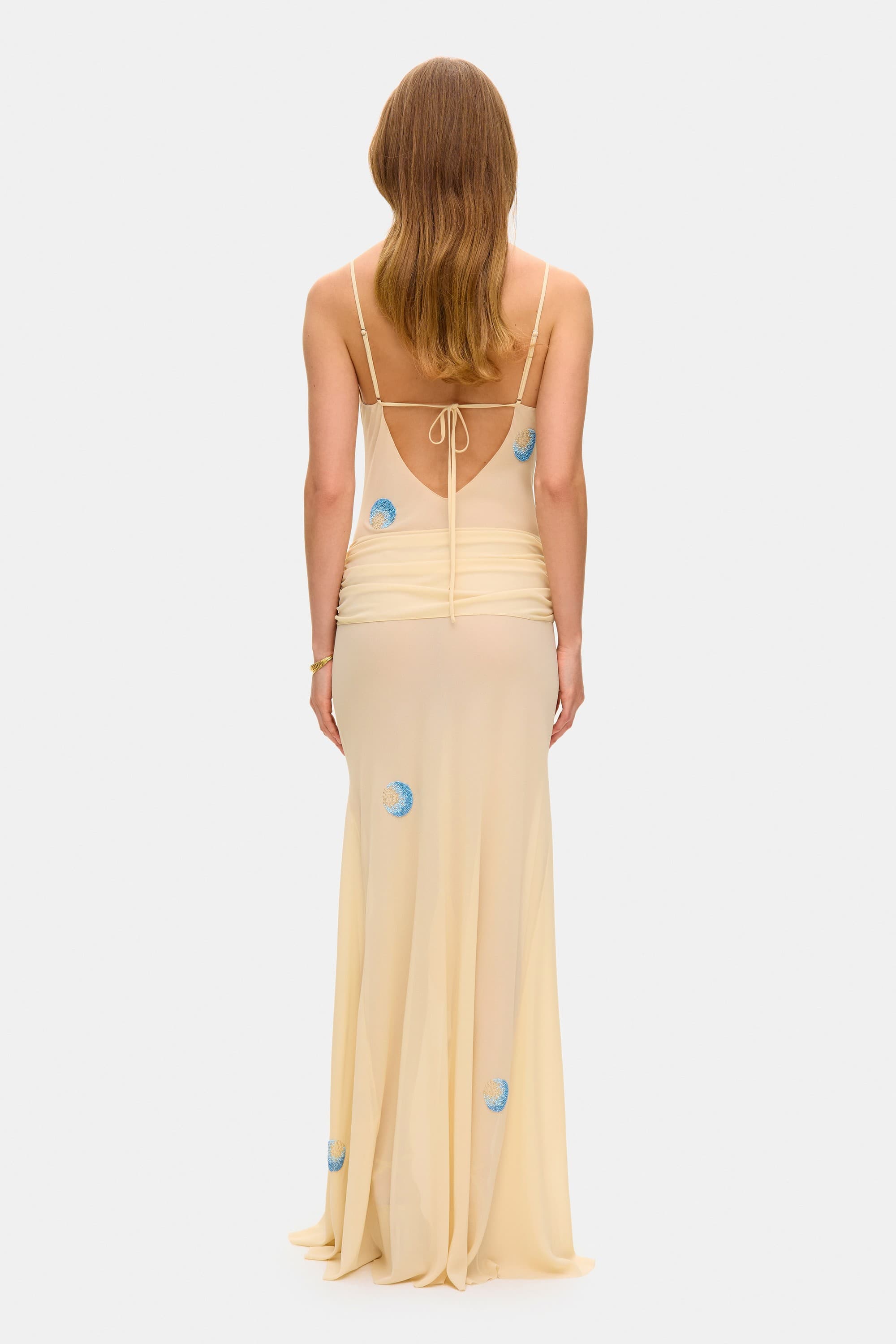Model in Zoe maxi dress with decorative scarf at the hips, featuring embroidery elements throughout the dress back view