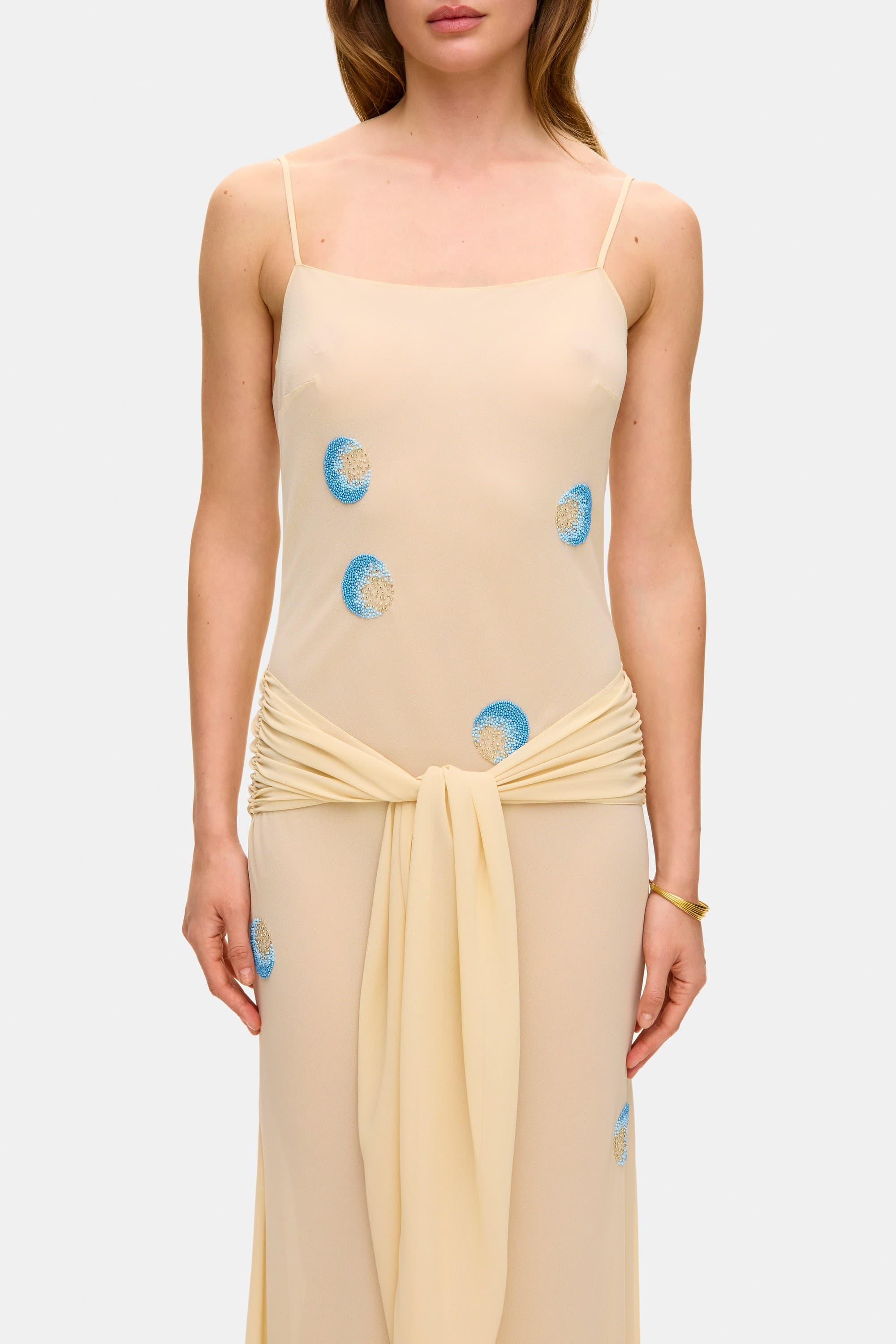 Model in Zoe maxi dress with decorative scarf at the hips, featuring embroidery elements throughout the dress front details view