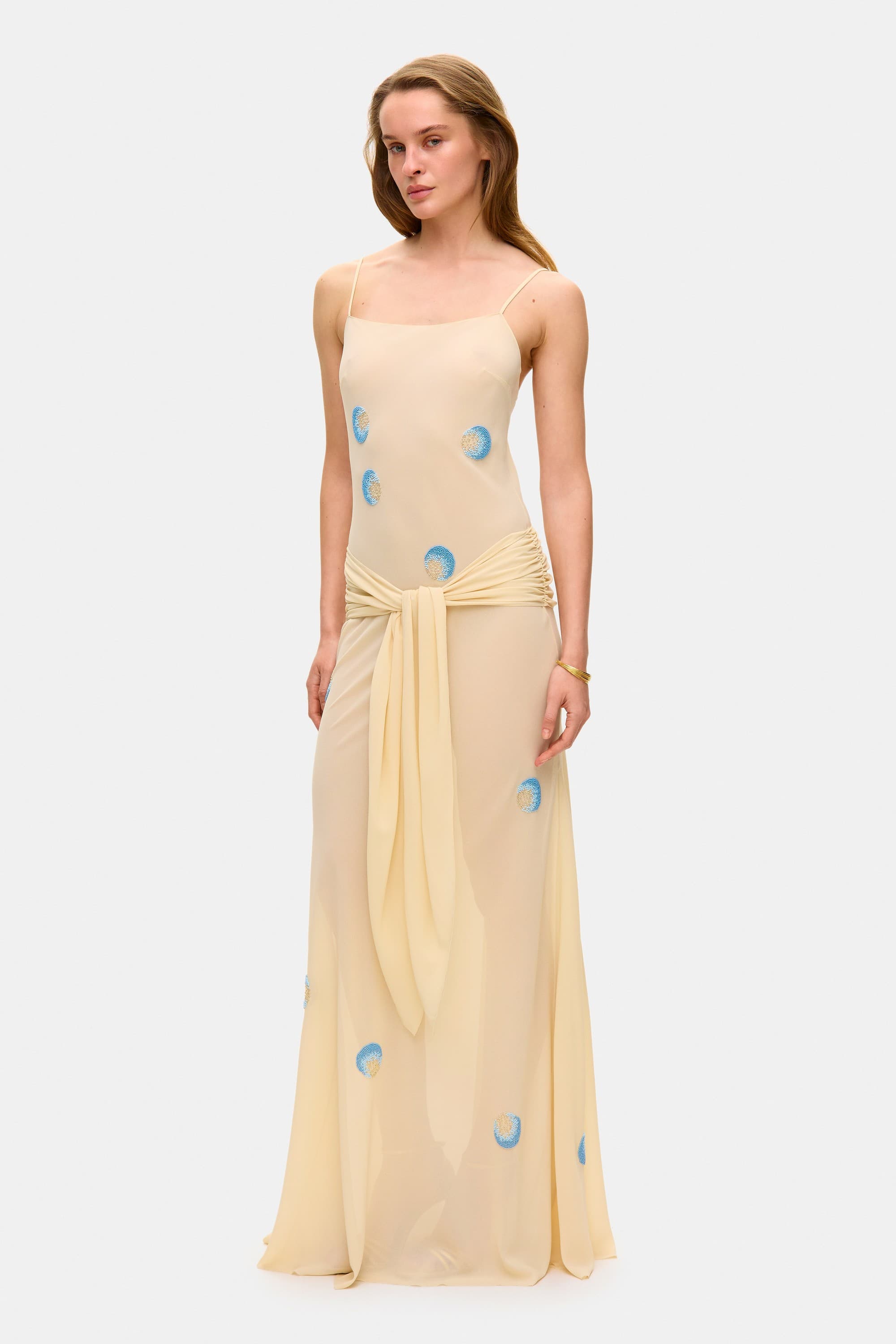 Model in Zoe maxi dress with decorative scarf at the hips, featuring embroidery elements throughout the dress side view