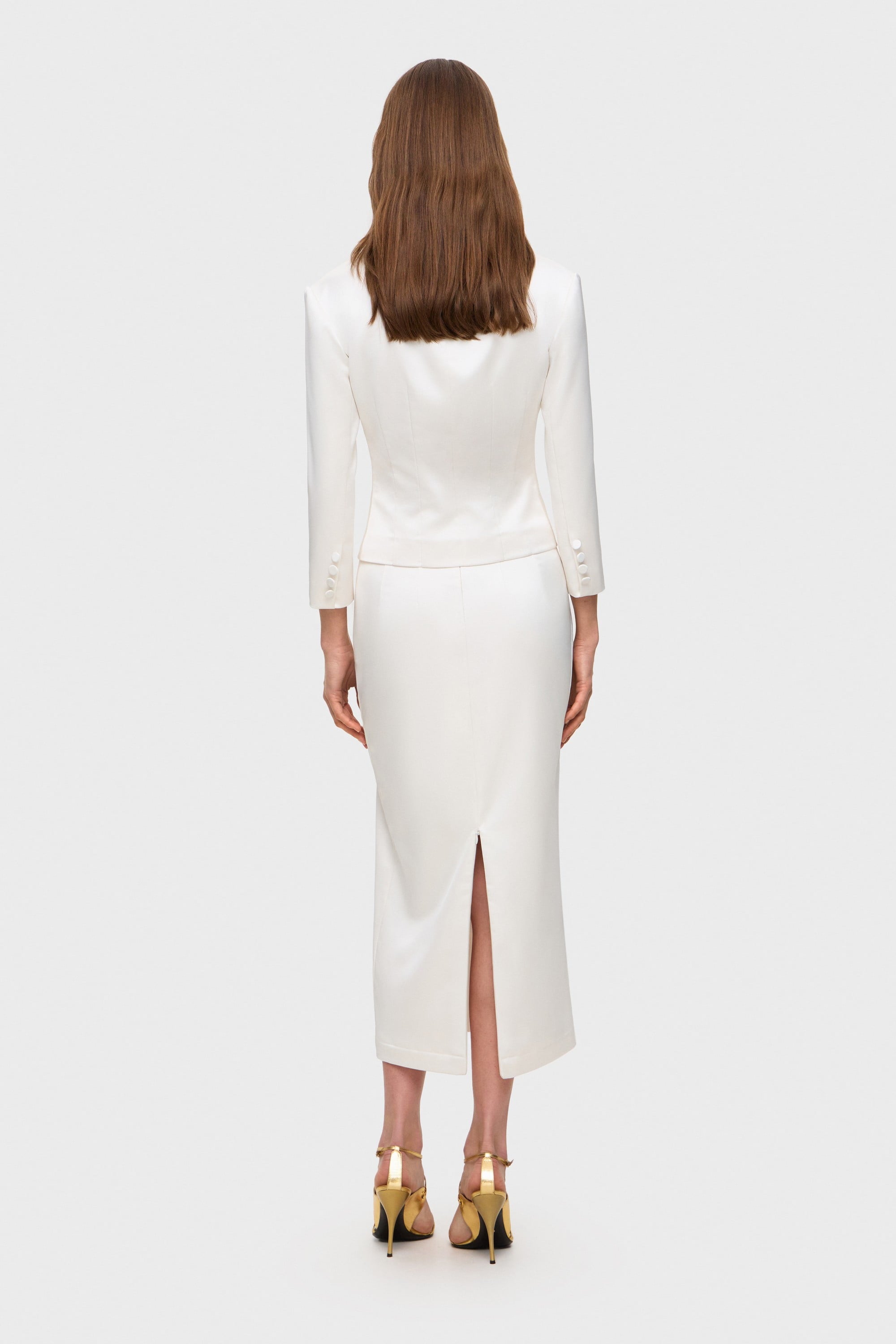 Woman wearing a white Giada jacket and Kaya skirt on a white background, back view