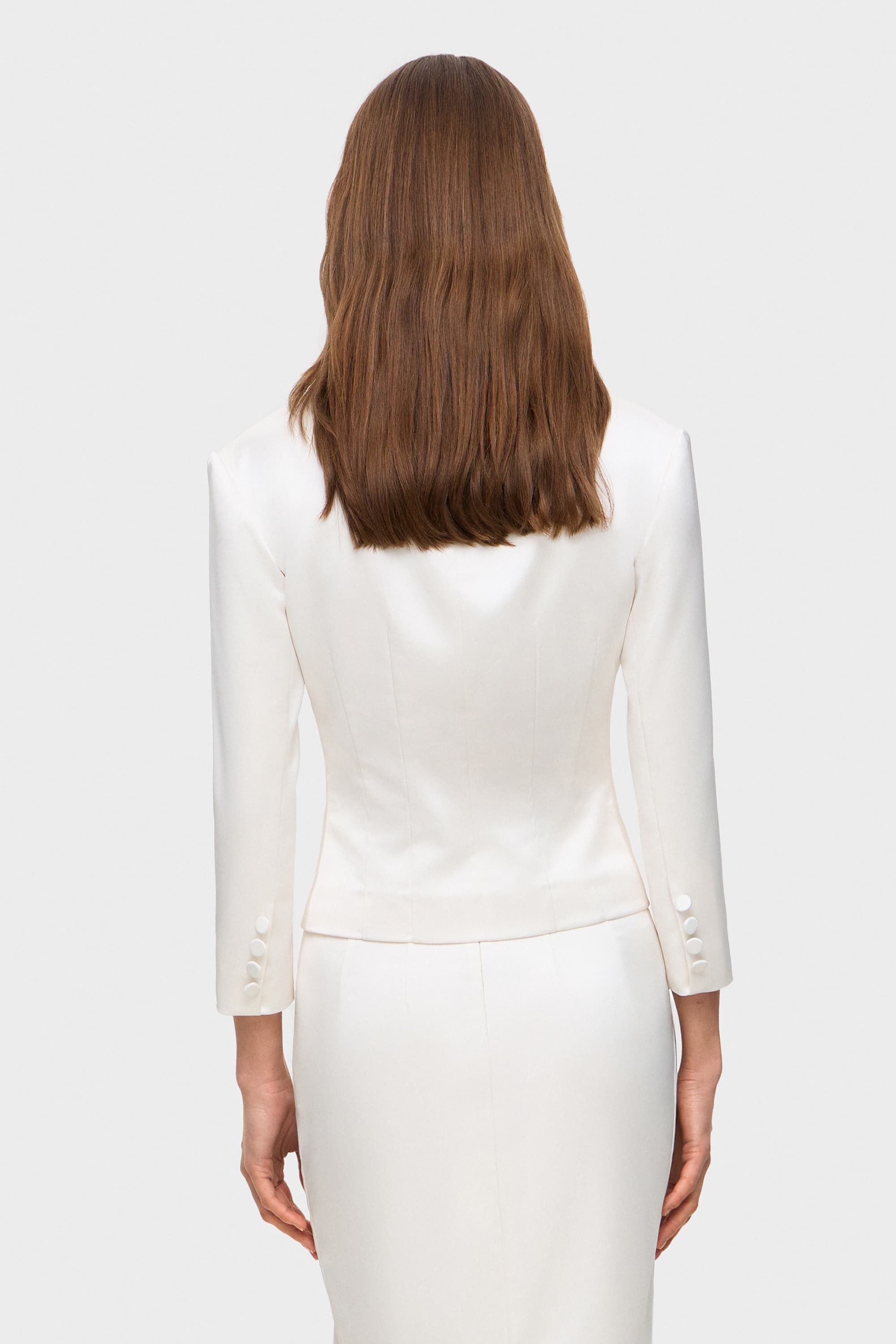 Woman wearing a white suit on a plain background, back view