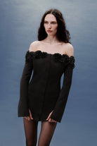 Woman wearing a black off-shoulder Micaela dress with floral details against a gray background