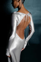 Woman wearing a silver Margit dress against a dark background, back view
