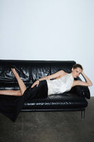 Woman wearing a two-tone Ayla dress with a white top and black skirt lying on a black leather couch against a plain wall