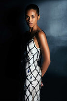 Woman wearing a ivory and black netted patterned with thin straps Helena dress on a black background, side view