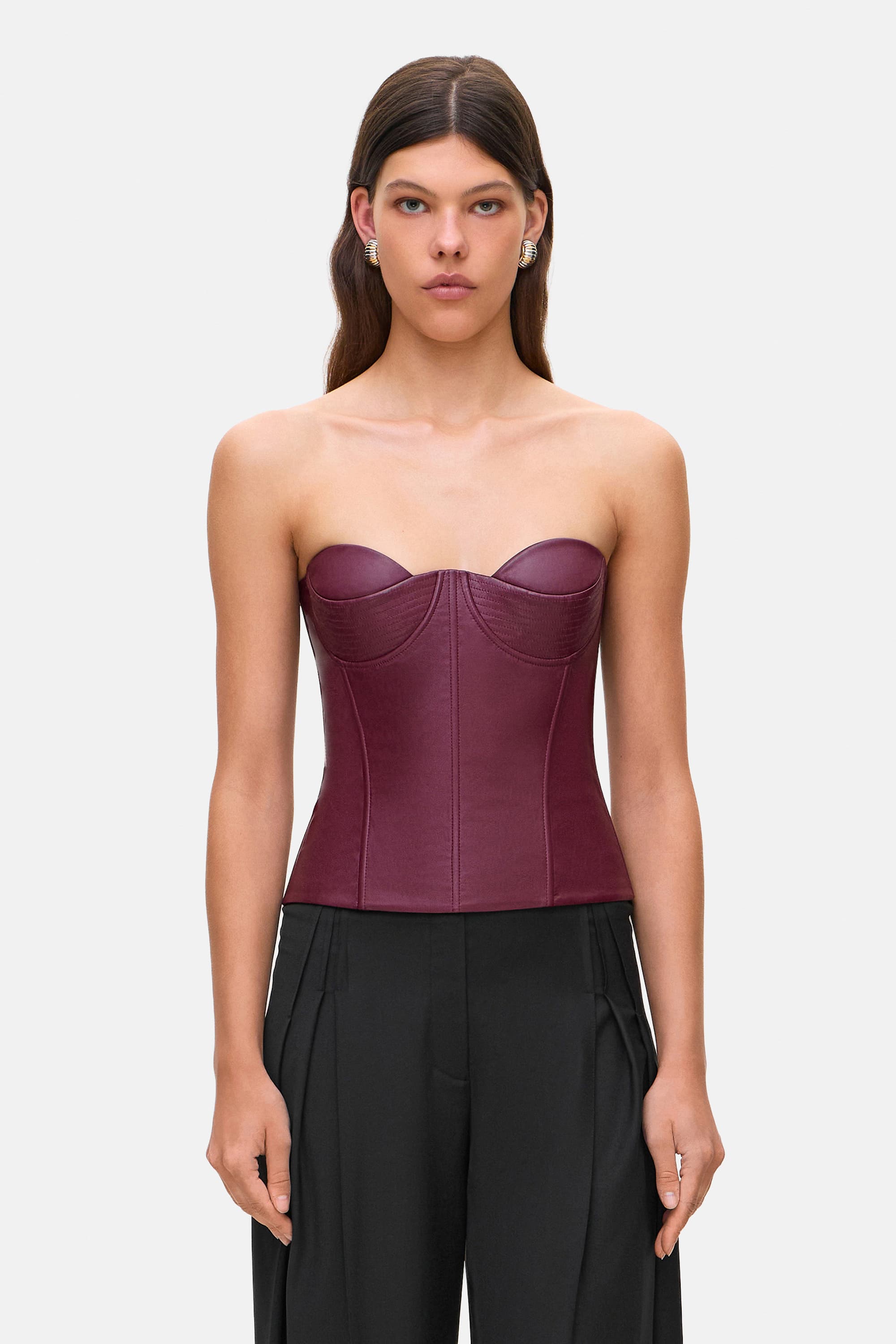 Woman wearing a strapless burgundy Susana corset and black pants on a white background, front view