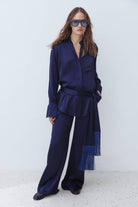 A model wearing a dark navy blue satin long-sleeve Lydia blouse and matching wide-leg Katerina trousers, styled with sunglasses and a matching fringed scarf, against a plain white studio background