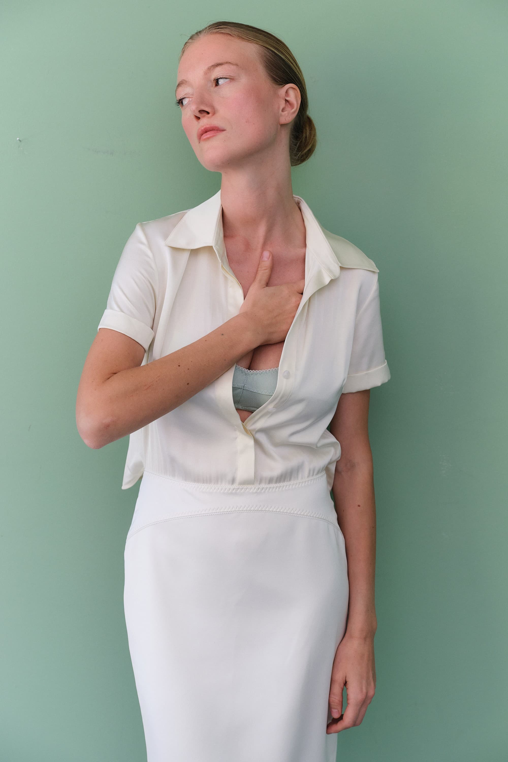 Woman wearing a white Arisa dress with a slit skirt and black belt against a light green background, front view