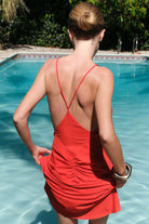 Woman in a coral Eliana dress standing by a pool, back view