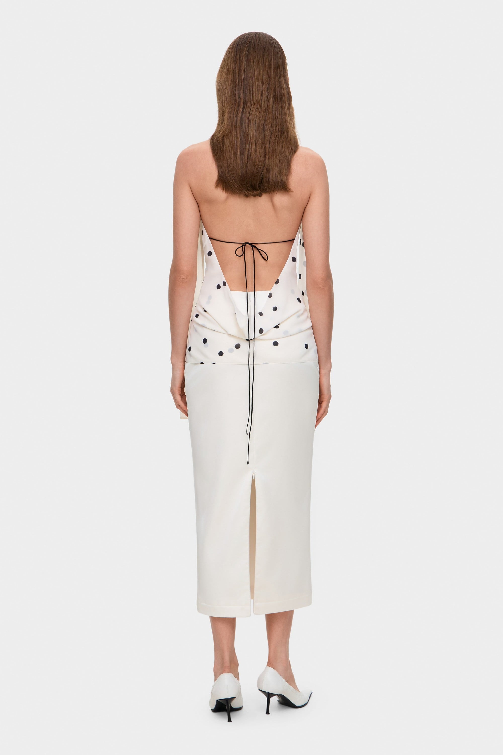 Woman wearing a white sleeveless Agnes top with black polka dots on a white background, back view